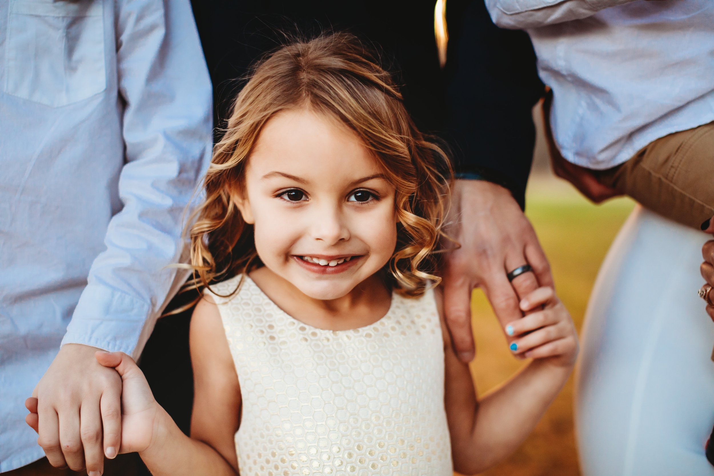  Young girl with curled hair smiles while holding her parent's hand on their wedding day by Teala Ward Photography. girl in wedding flower girl #tealawardphotography #tealawardweddings #LaSalleIllinois #IronwoodontheVermillion #weddingphotographyIL 