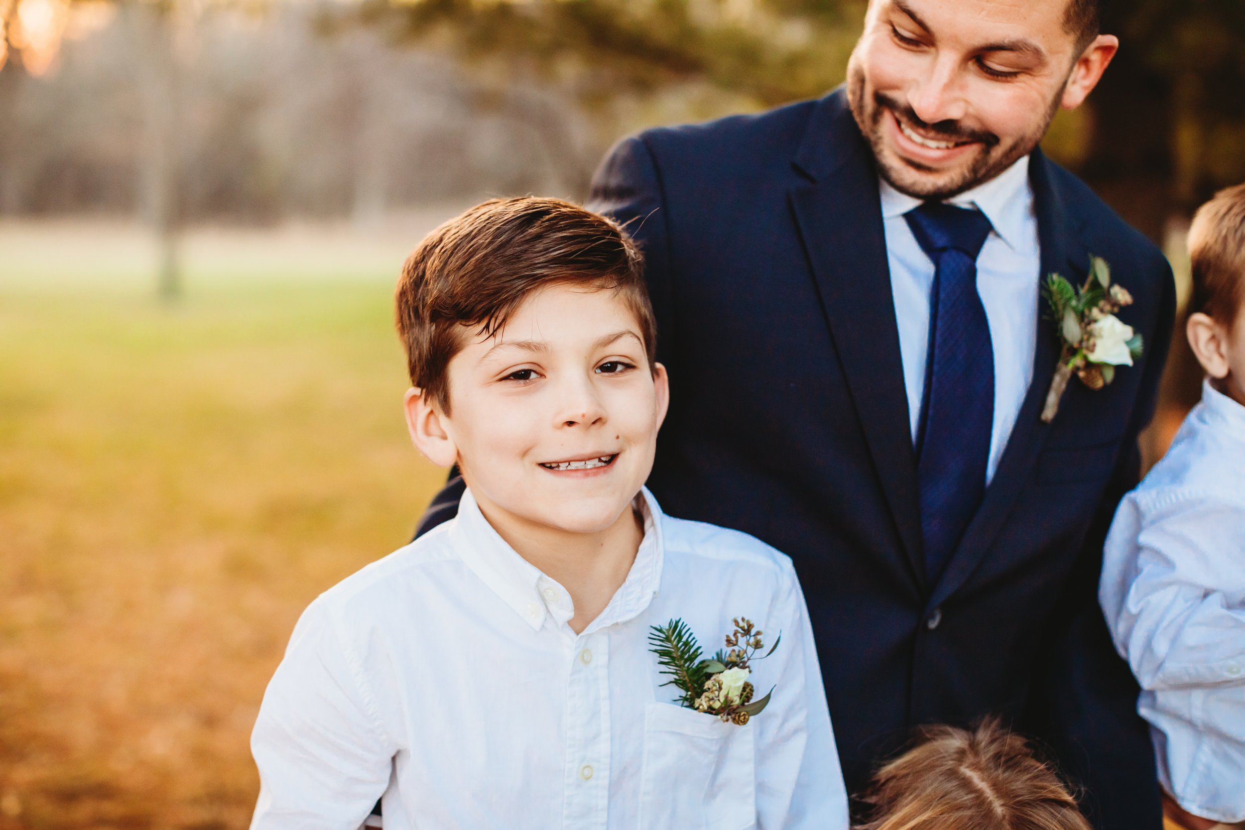  A boy smiles with his dad the groom at Ironwood on the Vermillion in IL by Teala Ward Photography. Son and groom navy tie winter wedding flowers #tealawardphotography #tealawardweddings #LaSalleIllinois #IronwoodontheVermillion #weddingphotographyIL