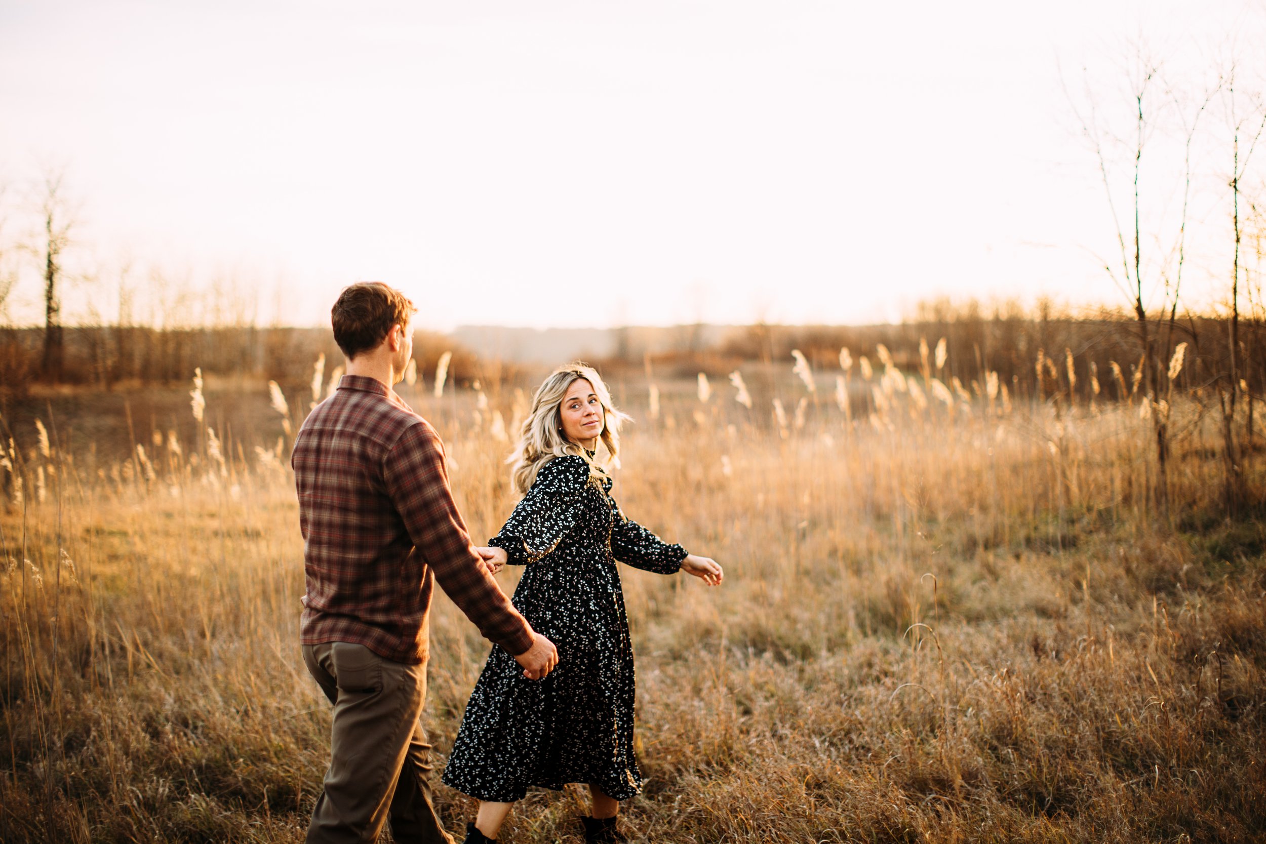 A married couple walks holding hands in a sunlit yellow grass field by Teala Ward Photography. Utica family photog warm rich edit #TealaWardPhotography #TealaWardFamilies #StarvedRockStatePark #BuffaloRockPhotographers #UticaIllinoisphotographers 