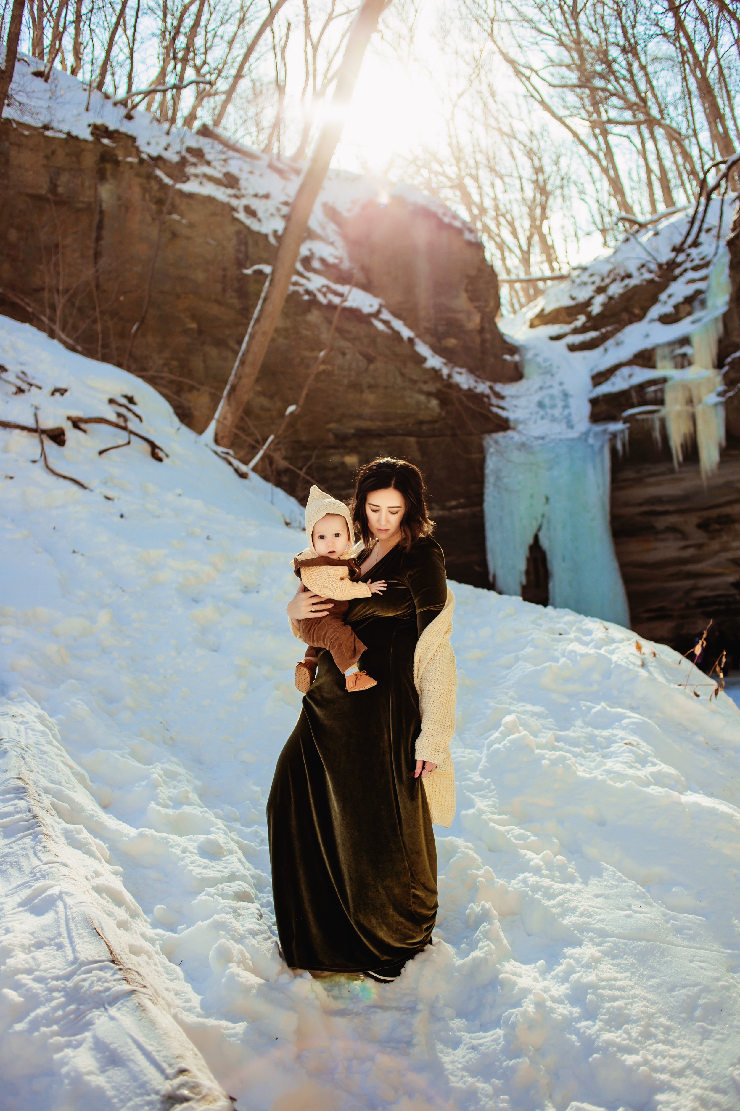  Teala Ward Photography captures a mother walking down a snowy hill with her child in her arms. winter motherhood photography #TealaWardPhotography #TealaWardNursing #StarvedRockStatePark #nursingbaby #breastfedbabyphotography #motherandbaby 