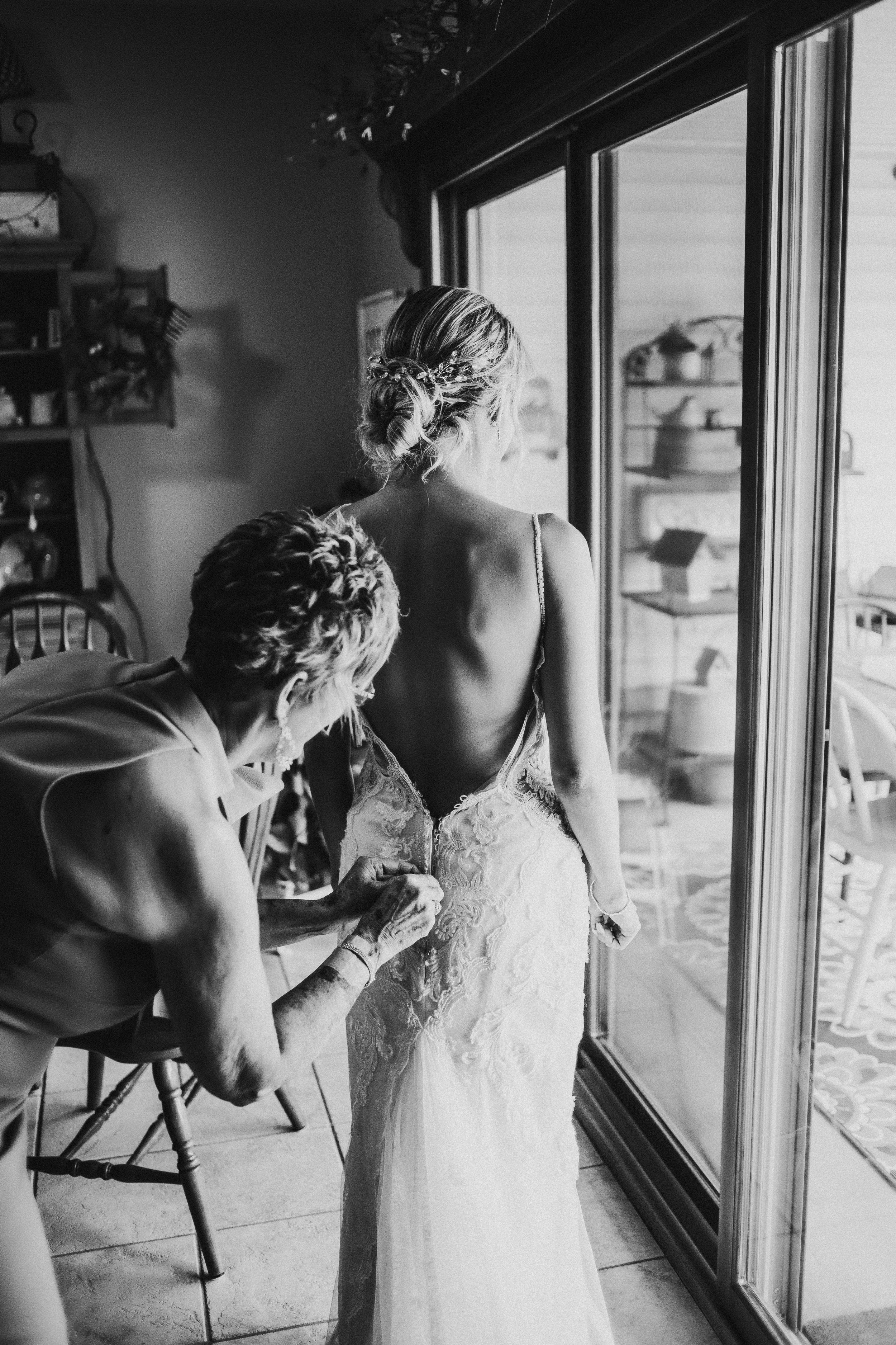  Mother of the bride helps the bride zip into her low backed lace wedding dress. updo at home casual wedding intimate ceremony #TealaWardPhotography #illinoisphotographer #princetonillinois #weddingphotographer #intimatewedding 