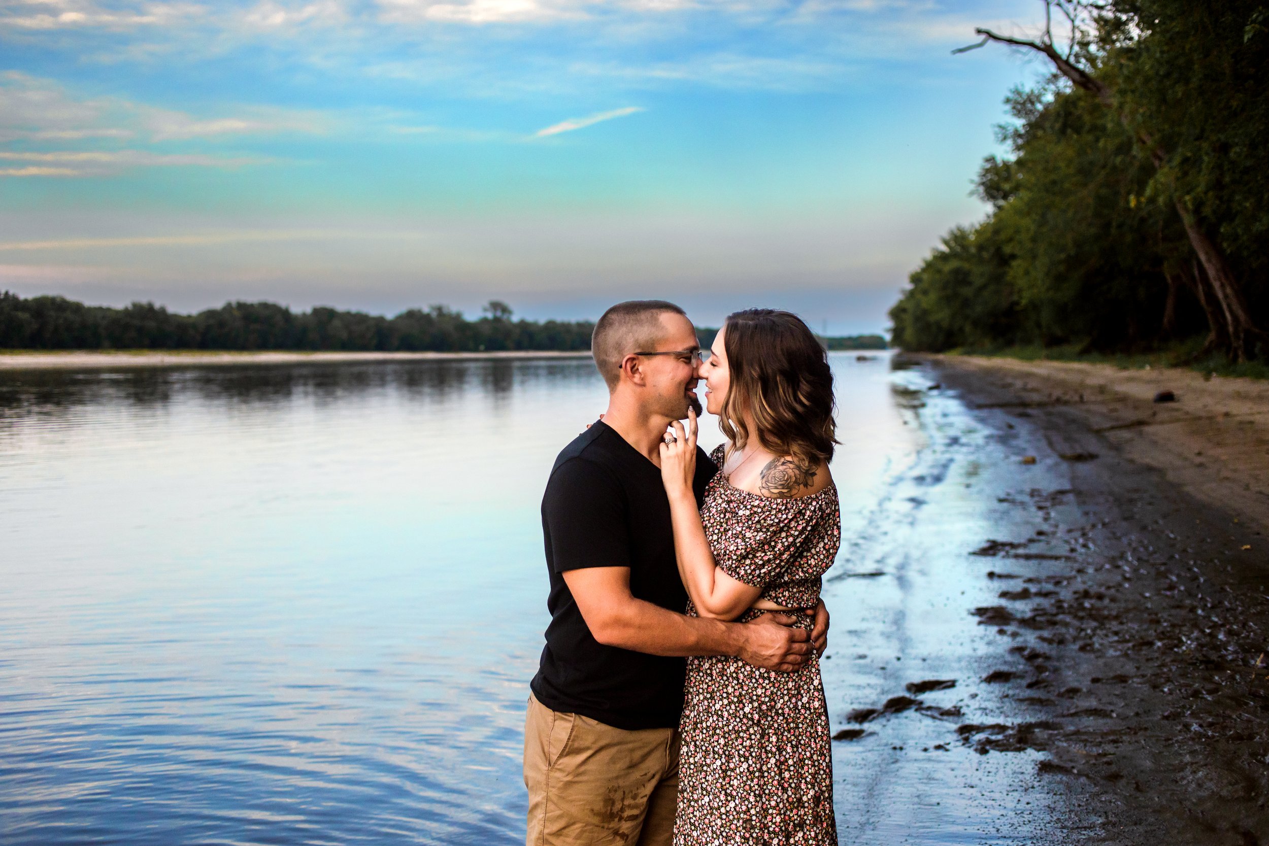  Husband and wife kiss next to a river with stunning sunset sky behind them by Teala Ward Photography. sunset kissing pictures #TealaWardPhotography #TealaWardFamilies #IllinoisRiverPhotography #IllinoisFamilyPhotography #familylifestylepics 
