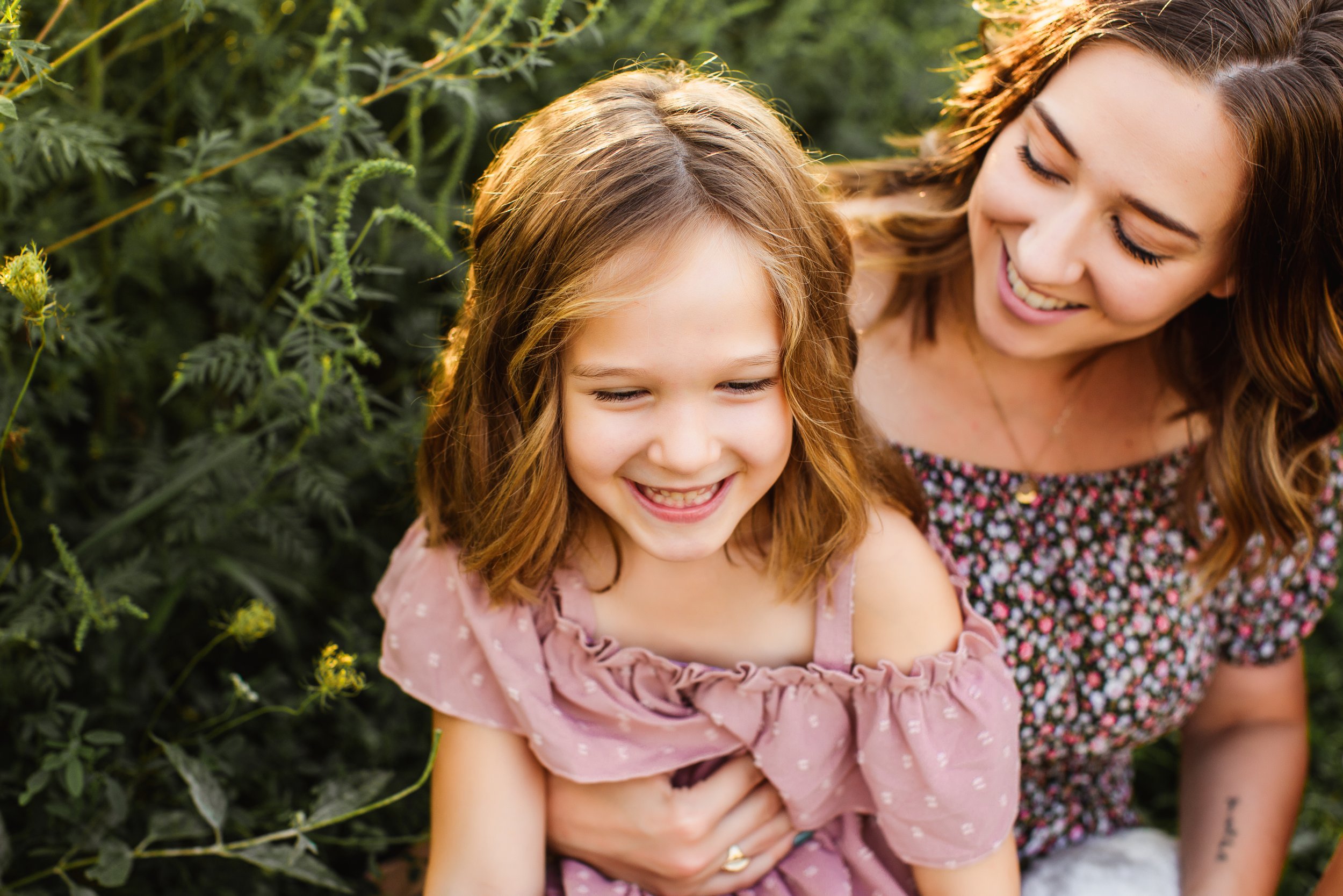  A little girl in a pink off-the-shoulder dress laughs with her mother captured by Teala Ward Photography. sunset pictures #TealaWardPhotography #TealaWardFamilies #IllinoisRiverPhotography #IllinoisFamilyPhotography #familylifestylepics 