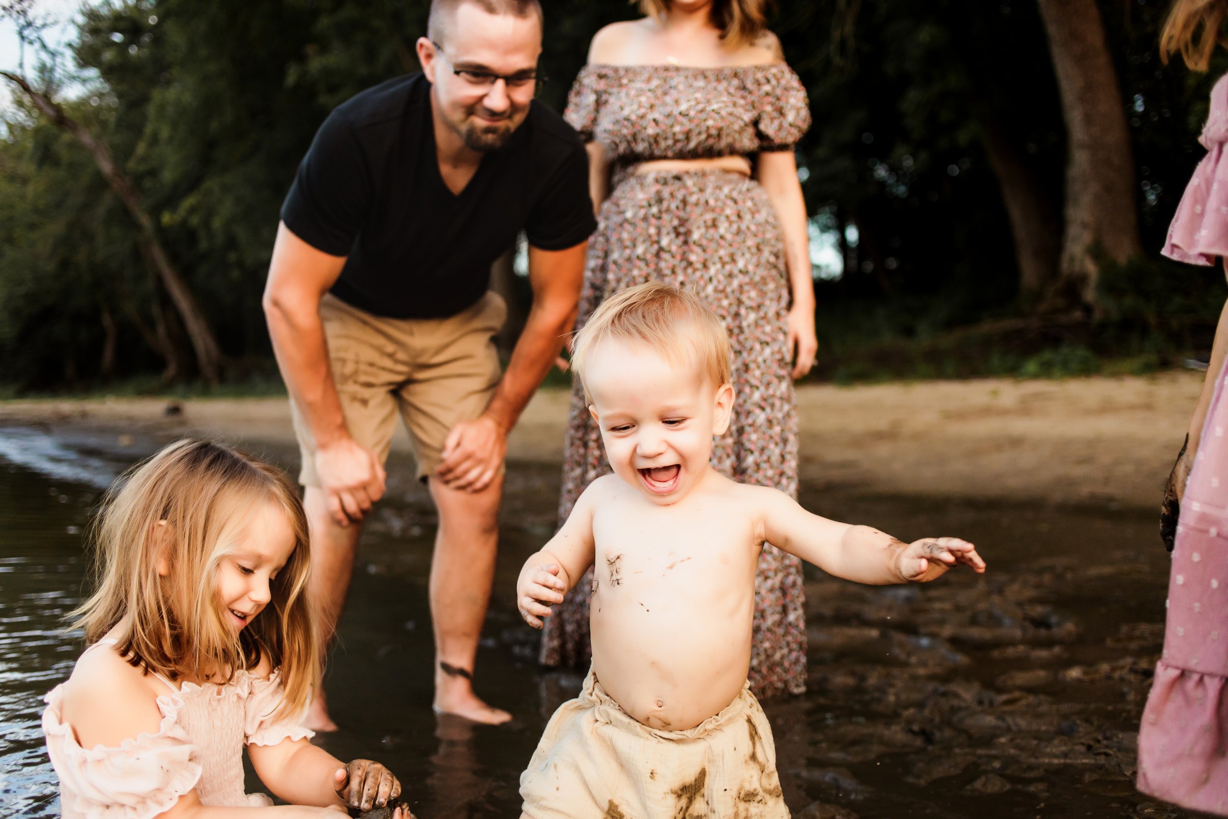  A muddy toddler boy laughs while playing in a river by Teala Ward Photography in Illinois. moody family portraits #TealaWardPhotography #TealaWardFamilies #IllinoisRiverPhotography #IllinoisFamilyPhotography #familylifestylepics 