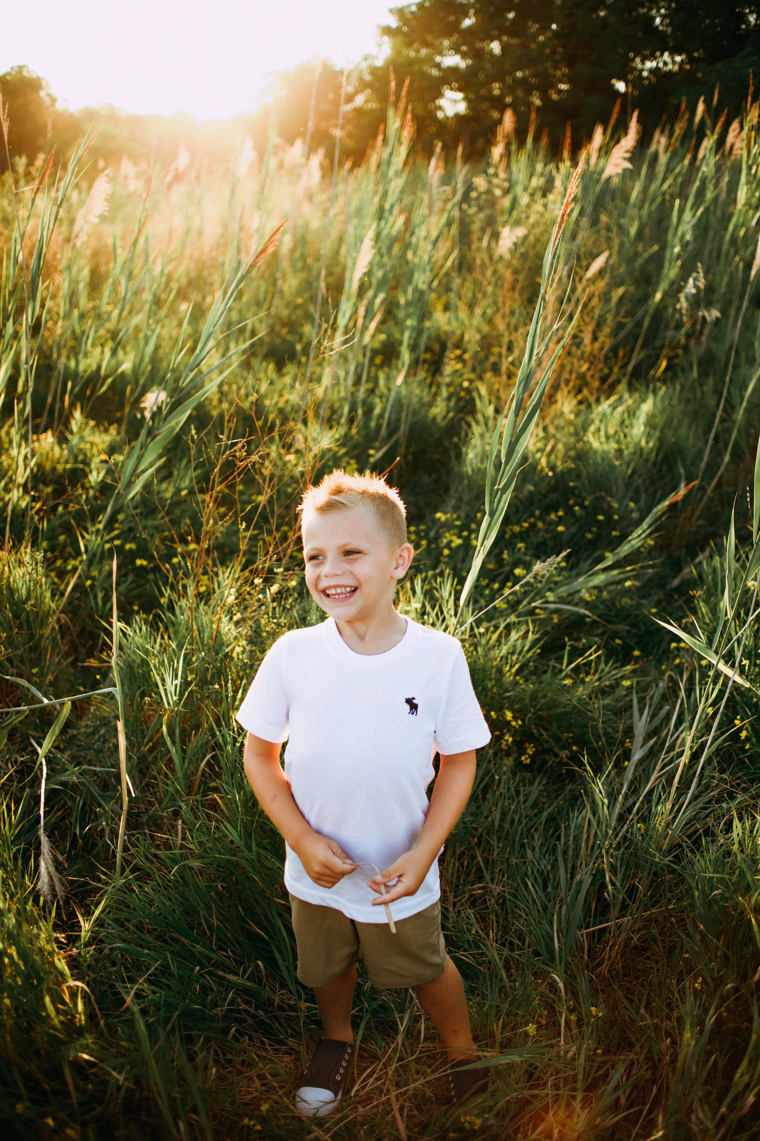  A young blonde hair boy wearing a white shirt smiles in a grass field by Teala Ward Photography. young boy portraits #motherhood #mommapics #TealaWardPhotography #TealaWardFamilies #IllinoisPhotographers #IllinoisFamilyPhotography 