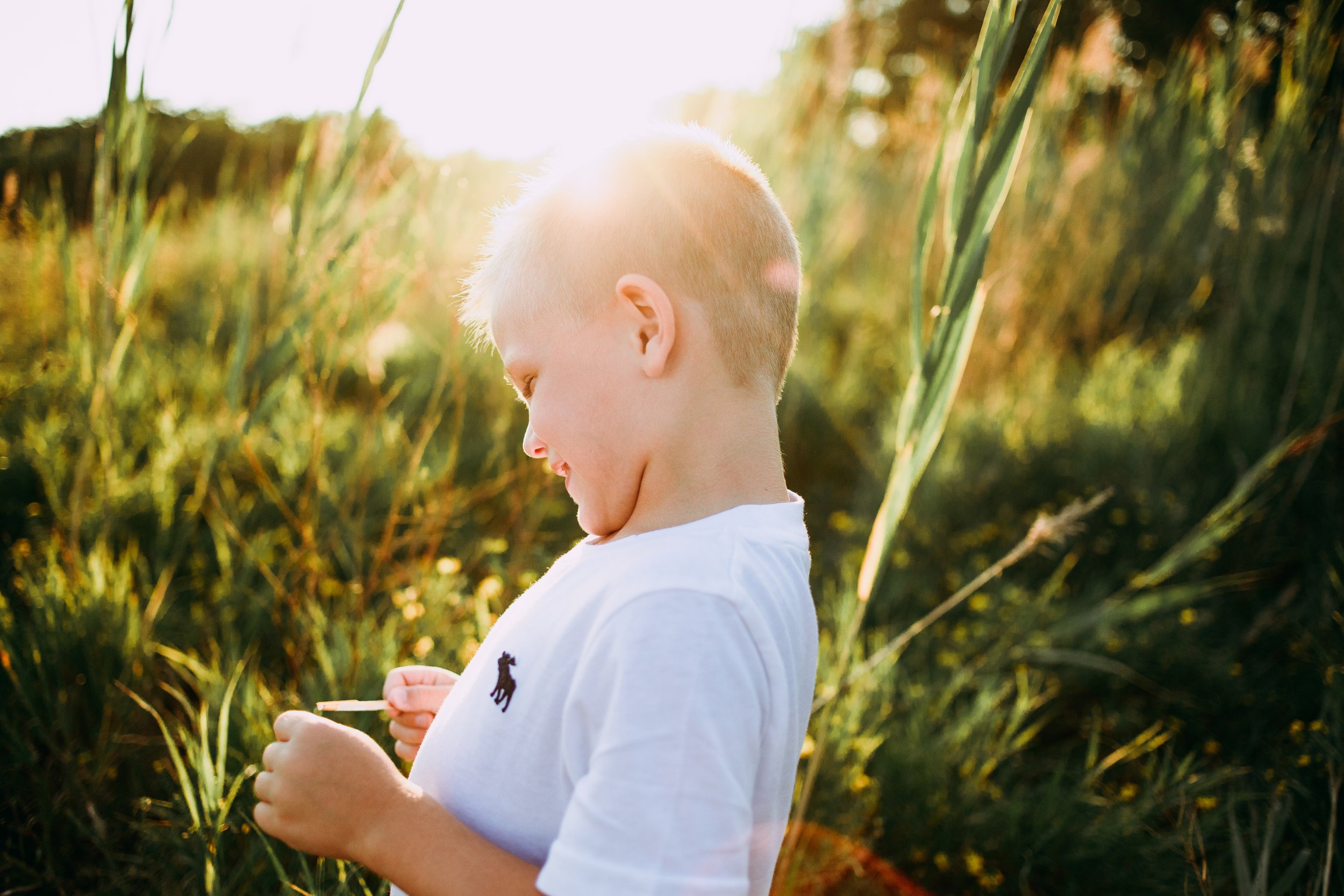  Teala Ward Photography captures a sunburst illuminating a little boy in a grass field in Illinois. Moody family portraits #motherhood #mommapics #TealaWardPhotography #TealaWardFamilies #IllinoisPhotographers #IllinoisFamilyPhotography 