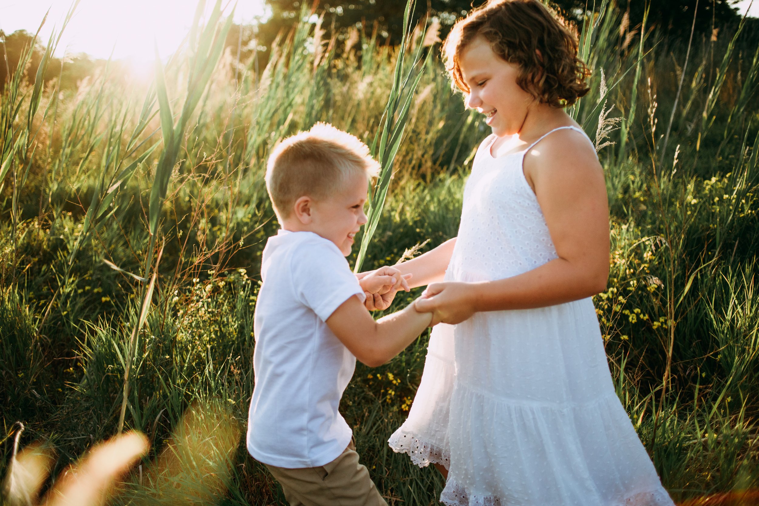  A brother and sister wearing white spin around in a grass field at sunset by Teala Ward Photography. sibling moment captured #motherhood #mommapics #TealaWardPhotography #TealaWardFamilies #IllinoisPhotographers #IllinoisFamilyPhotography 
