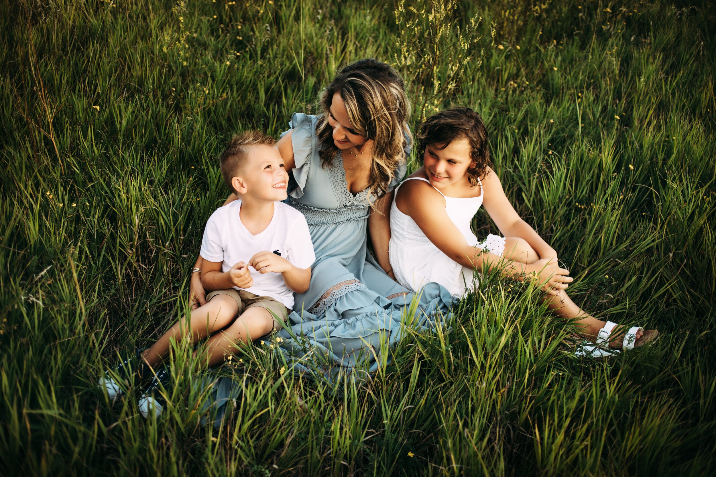 Sitting in a grass field a young family takes a family portrait by Teala Ward Photography in the Illinois Valley. sitting family pose #motherhood #mommapics #TealaWardPhotography #TealaWardFamilies #IllinoisPhotographers #IllinoisFamilyPhotography 