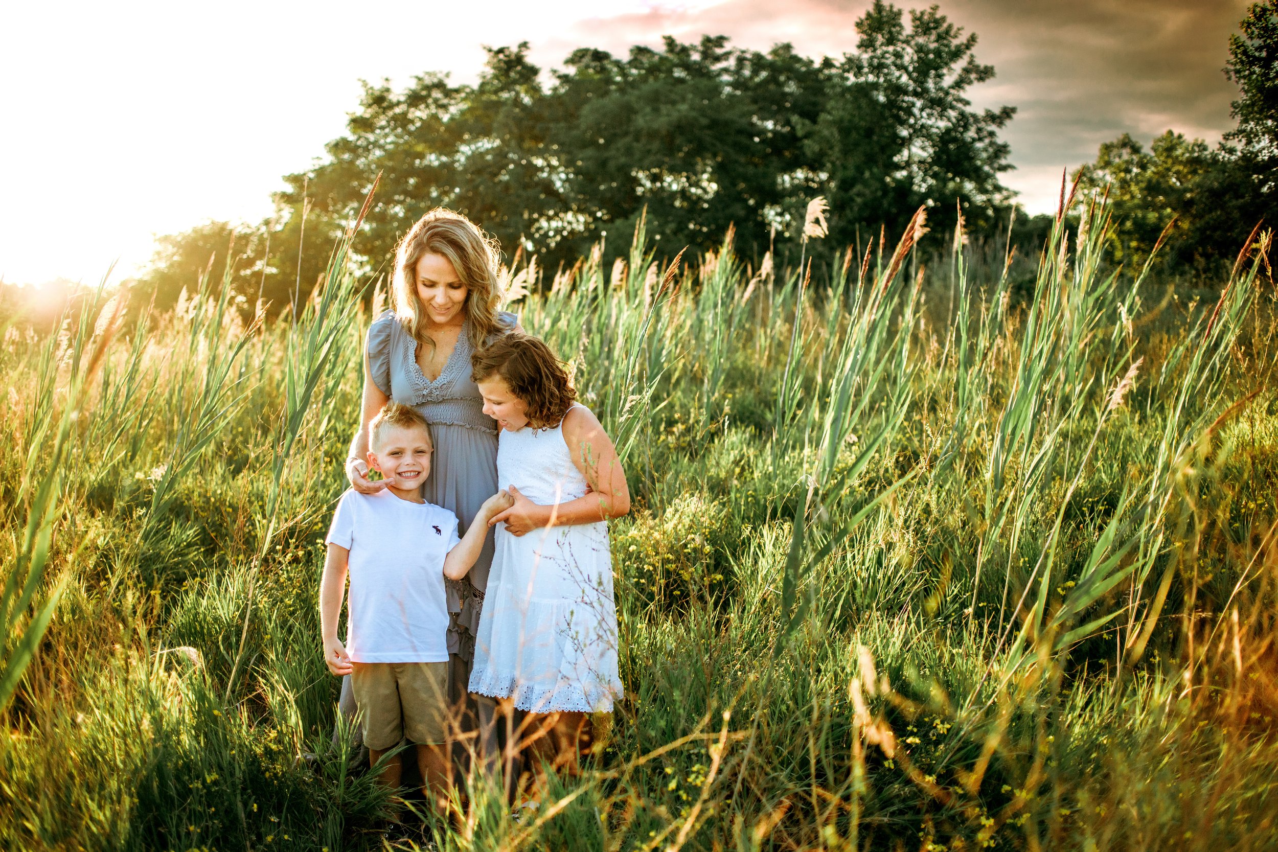  A mother and her children hug as sunshine kisses their skin and the grass around them by Teala Ward Photography. artistic pictures #motherhood #mommapics #TealaWardPhotography #TealaWardFamilies #IllinoisPhotographers #IllinoisFamilyPhotography 