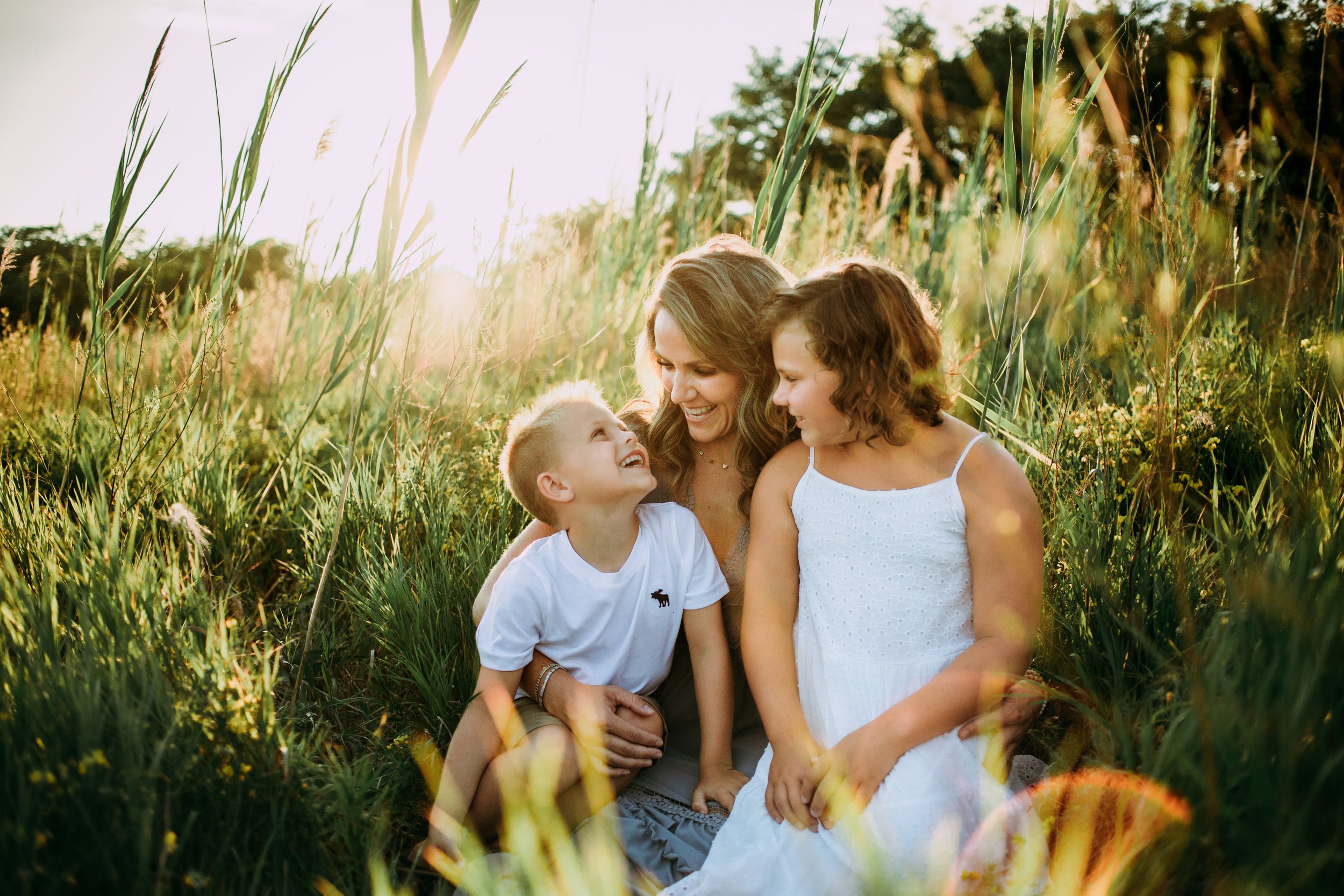  In the Illinois Valley at dusk, a family sits in a grass field laughing together by Teala Ward Photography. family outfit ideas #motherhood #mommapics #TealaWardPhotography #TealaWardFamilies #IllinoisPhotographers #IllinoisFamilyPhotography 