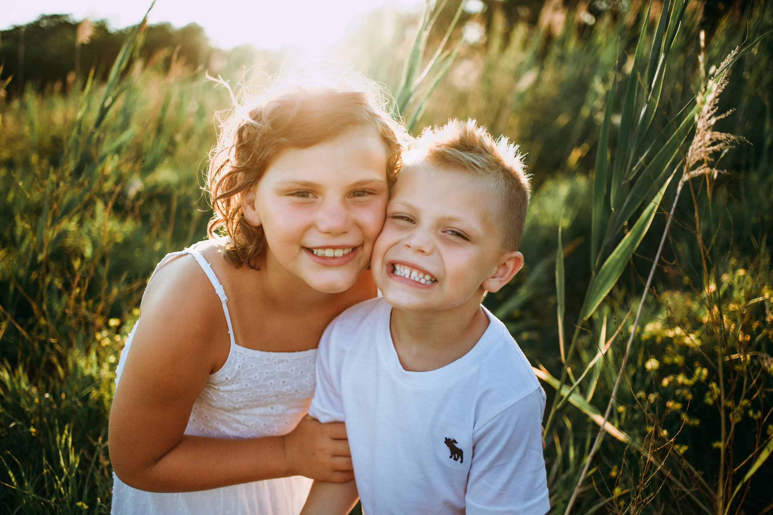  A brother and sister smoosh their heads together and smile with a sunset behind them by Teala Ward Photography. colorful family portrait #motherhood #mommapics #TealaWardPhotography #TealaWardFamilies #IllinoisPhotographers #IllinoisFamilyPhotograph