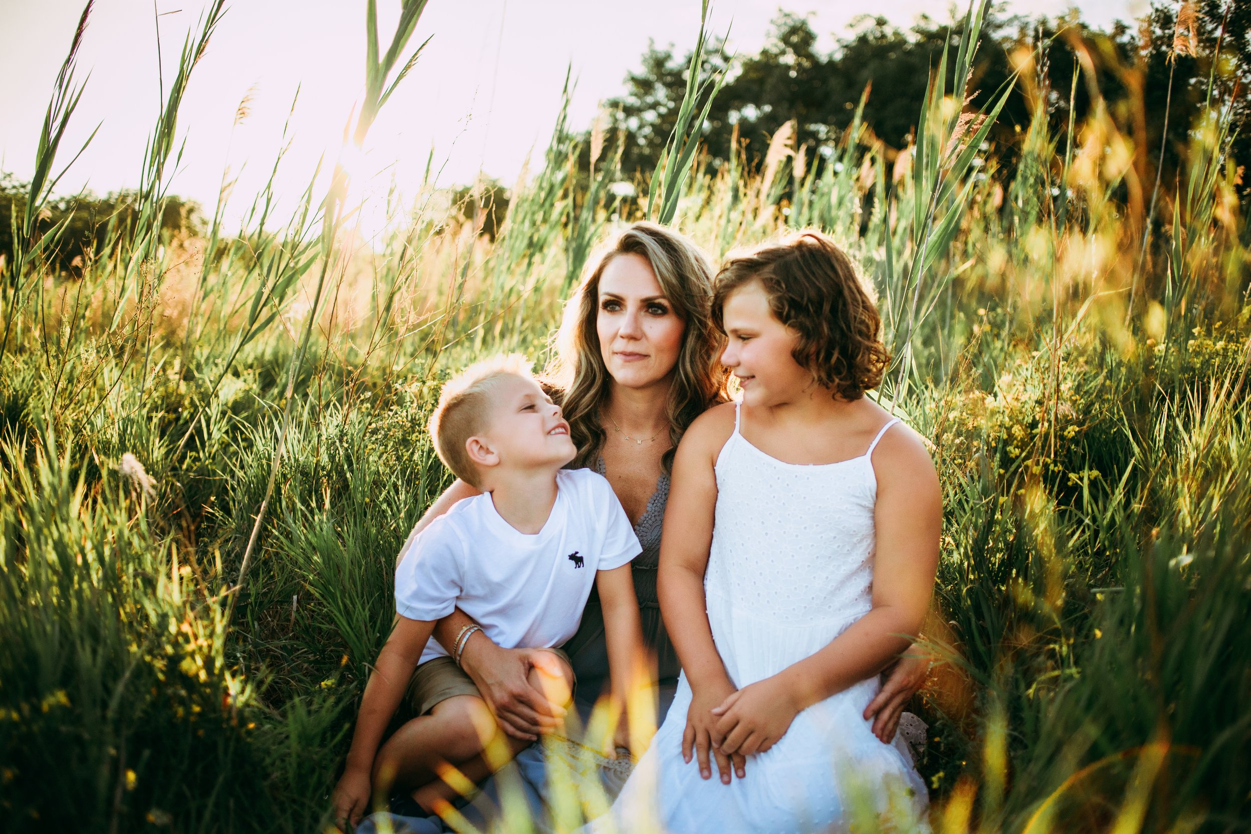  A mother sits in tall grass with her son and daughter by Teala Ward Photography in Illinois. Kids wearing white mother in dress #motherhood #mommapics #TealaWardPhotography #TealaWardFamilies #IllinoisPhotographers #IllinoisFamilyPhotography 