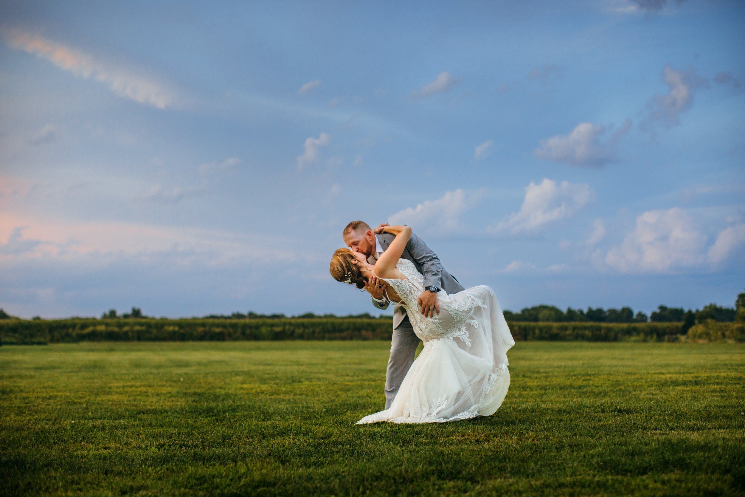  The groom dips the bride and kisses her in a green valley with blue skies by Teala Ward Photography. country wedding kissing #TealaWardPhotography #IllinoisValleyPhotographer #summerwedding #TealaWardWeddings #Illinoisweddings  