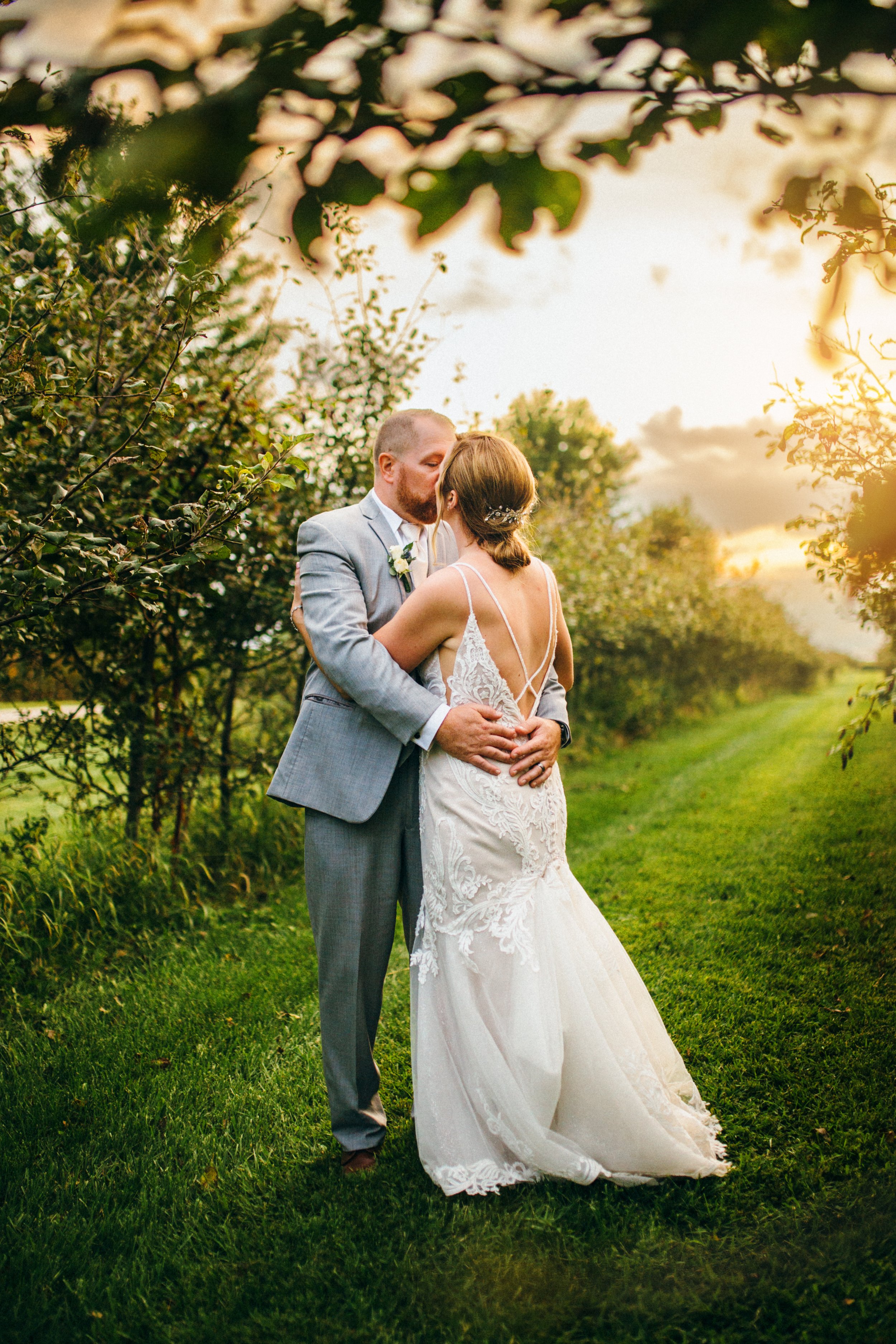  In an orchard at sunset, a bride and groom are caught kissing by wedding photographer Teala Ward Photography. summer wedding Illinois #TealaWardPhotography #IllinoisValleyPhotographer #summerwedding #TealaWardWeddings #Illinoisweddings  