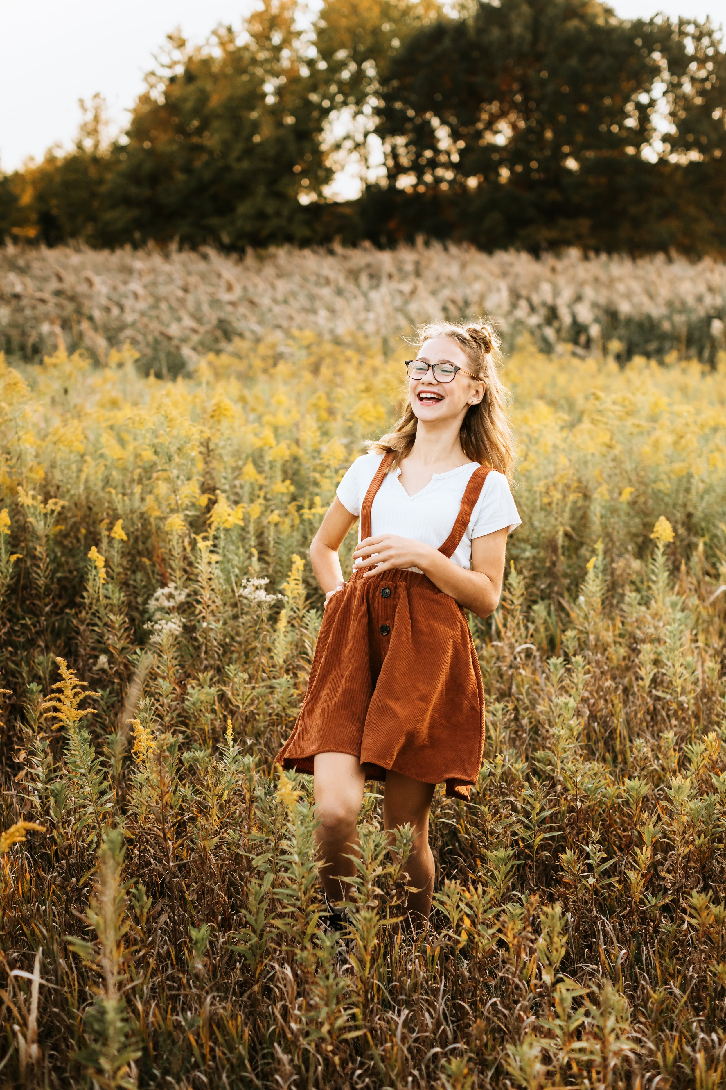  Teala Ward Photography captures a girl laughing in a yellow grass field wearing glasses and a jumper. Illinois Valley photog #TealaWardPhotography #TealaWardFamilies #IllinoisValleyfamilypics #fursibiling #Illinoisfamilyphotography #brother&amp;sist