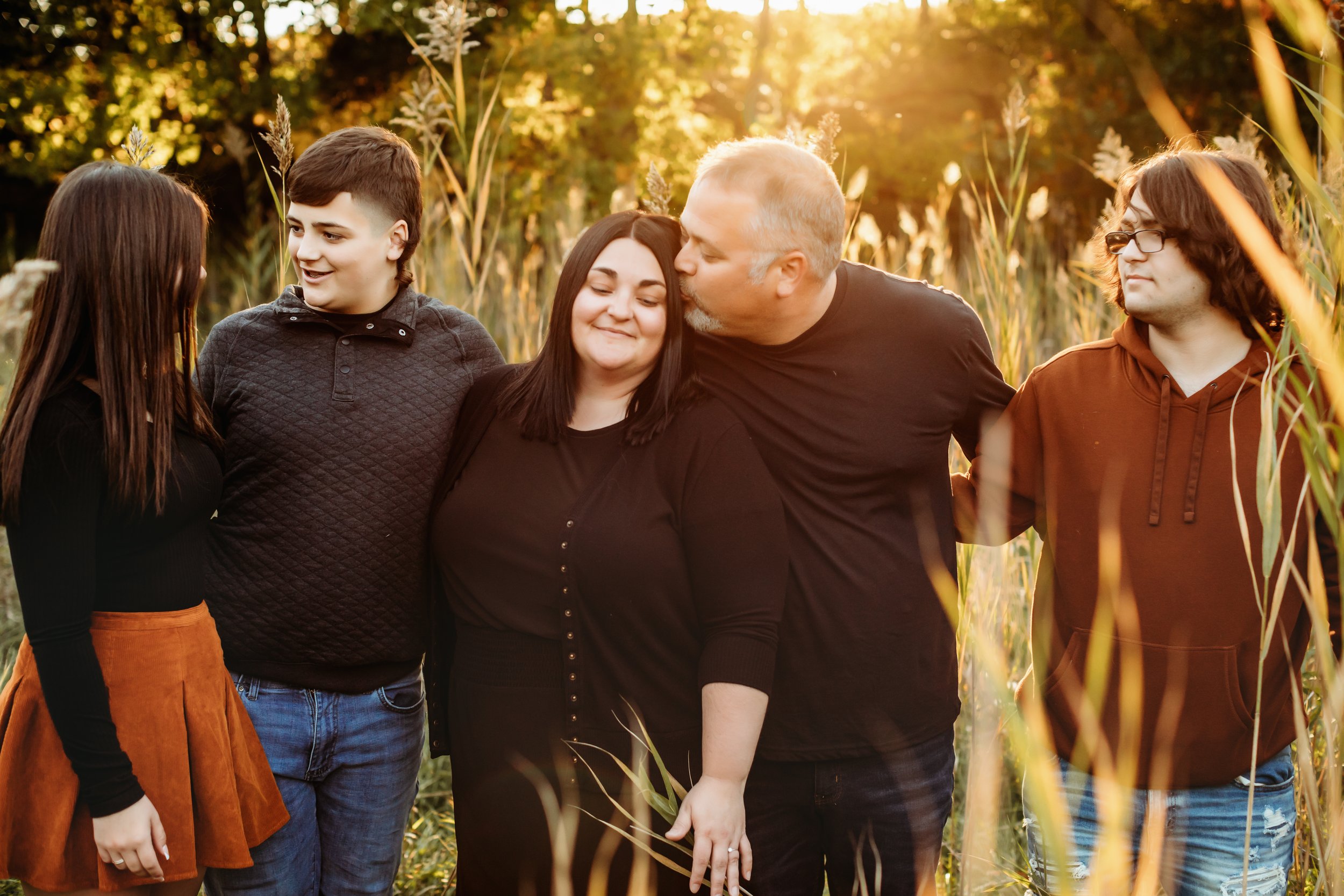  Family portrait with the sun setting behind them and yellow grass surrounding them by Teala Ward Photography.  Golden family portraits three kids in black family outfits #TealaWardPhotography #TealaWardFamilies #Outdoorfamilyportraits #IllinoisPhoto