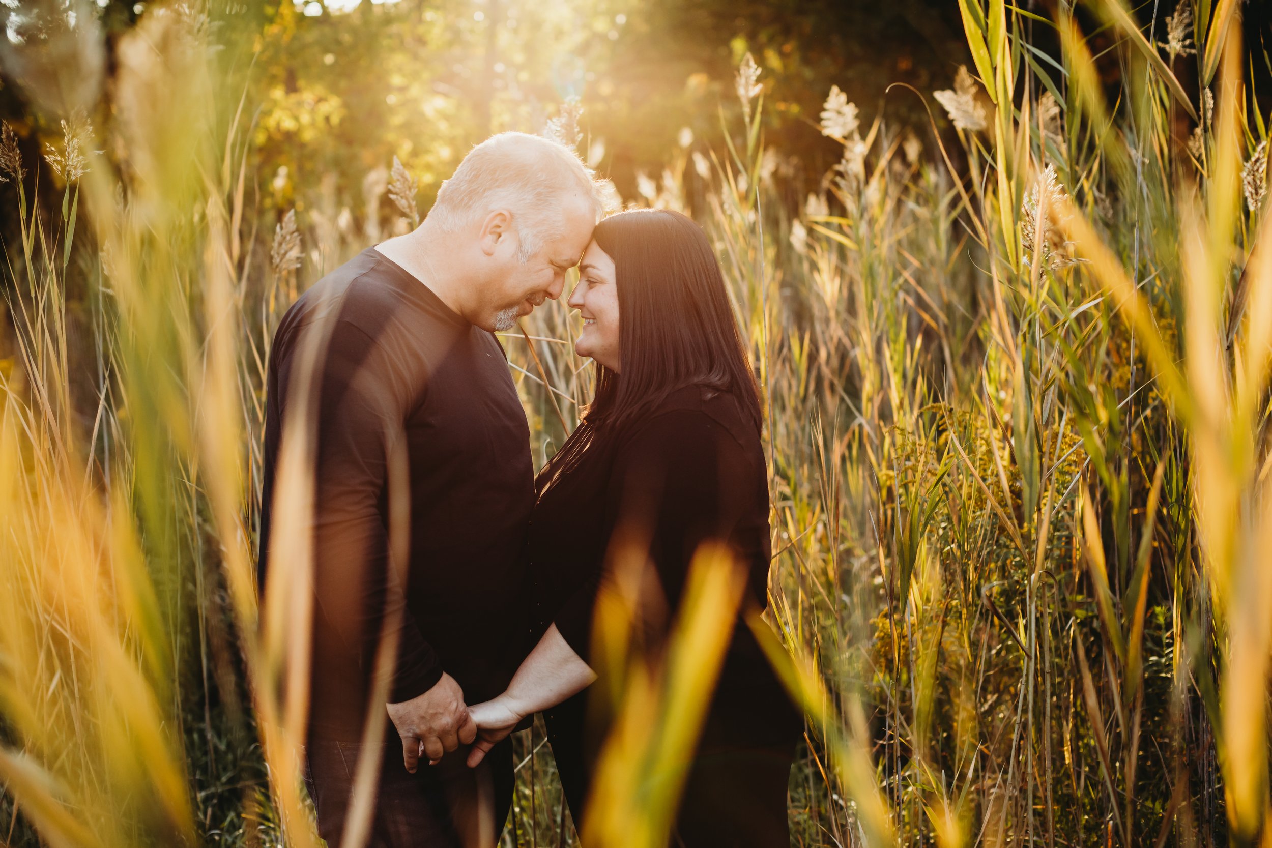  In a bright warm light field, a husband and wife put their foreheads together by Teala Ward Photography. husband and wife black outfits summer locations in Illinois #TealaWardPhotography #TealaWardFamilies #Outdoorfamilyportraits #IllinoisPhotograph