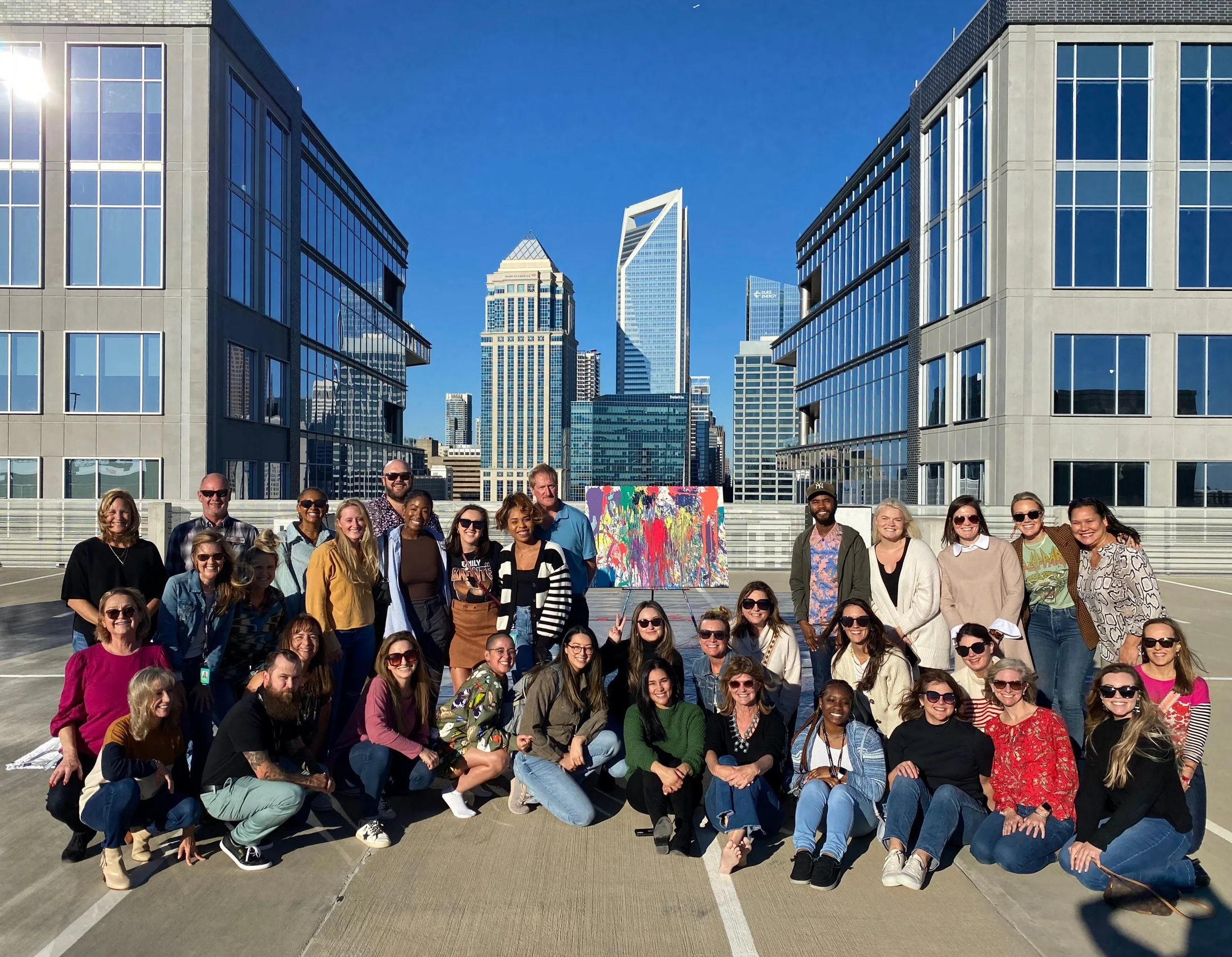 A large group around their finished canvas on a rooftop, uptown behind them.