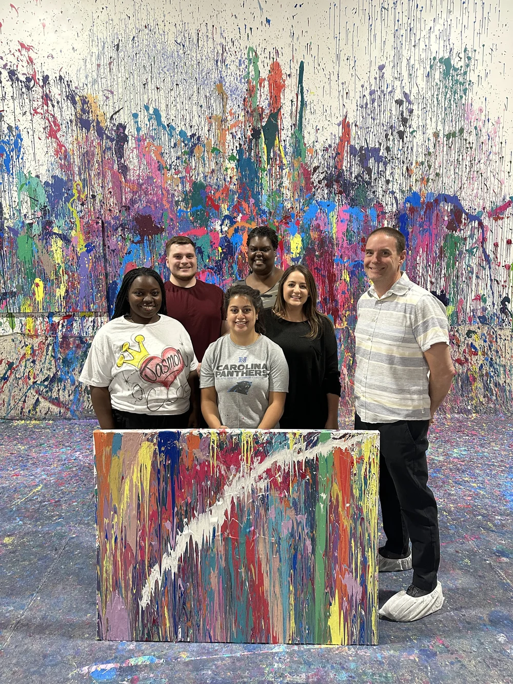A team behind their finished canvas, splattered wall behind them.