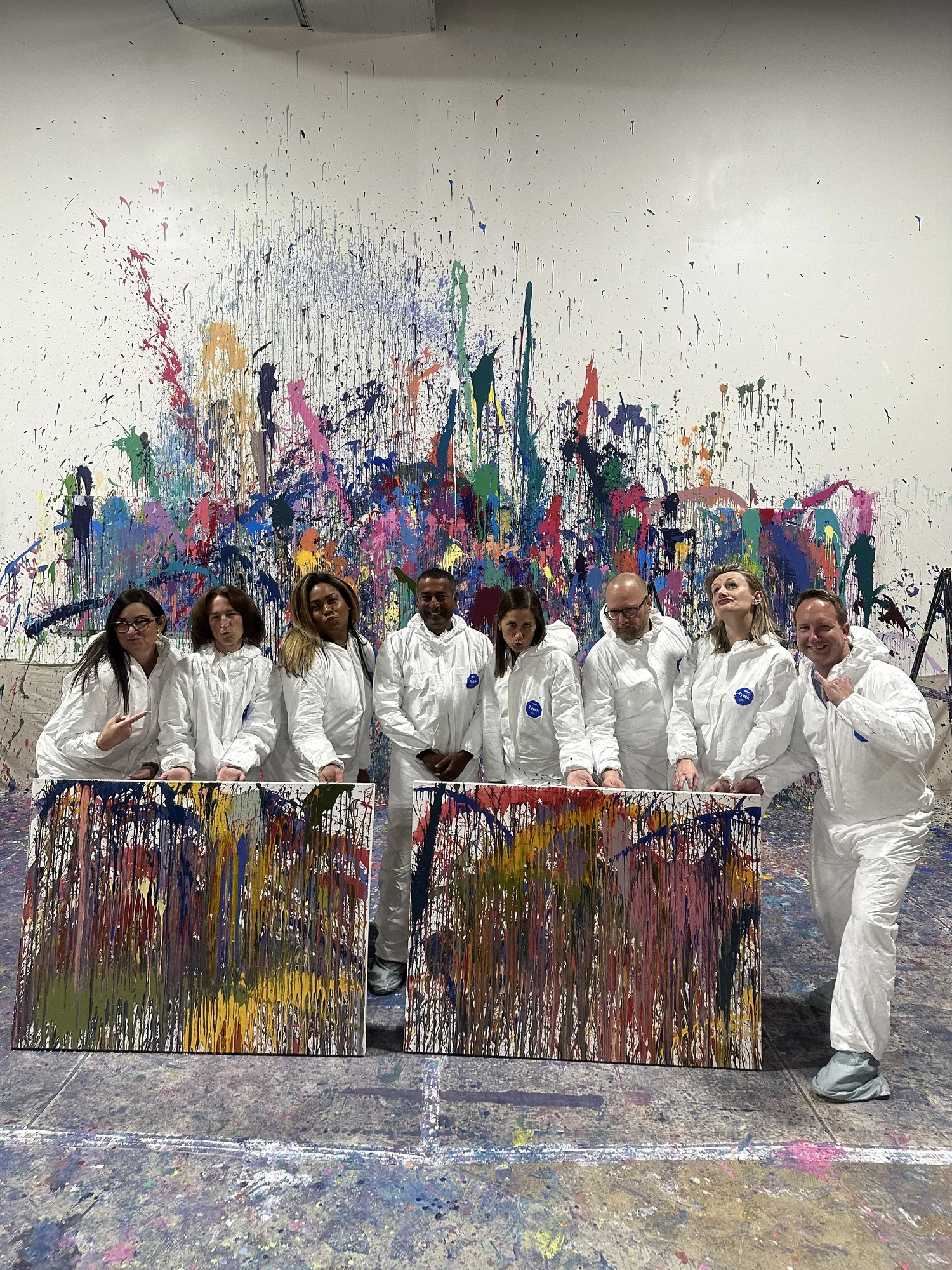 A team in matching coveralls behind two finished canvases in the studio.