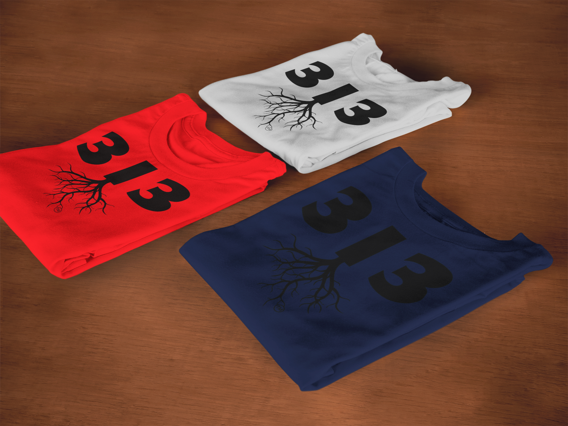 T-SHIRT MOCKUP OF THREE FOLDED 313 AREA CODE T-SHIRTS (GREY, RED, NAVY BLUE) LYING ON TOP OF A WOODEN SURFACE.png