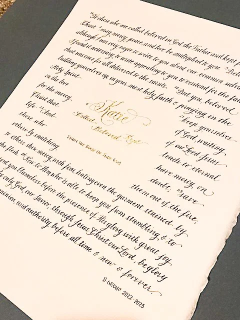 Close-up of an elegant, handwritten certificate with gold embellishment and decorative script, presented on textured paper.