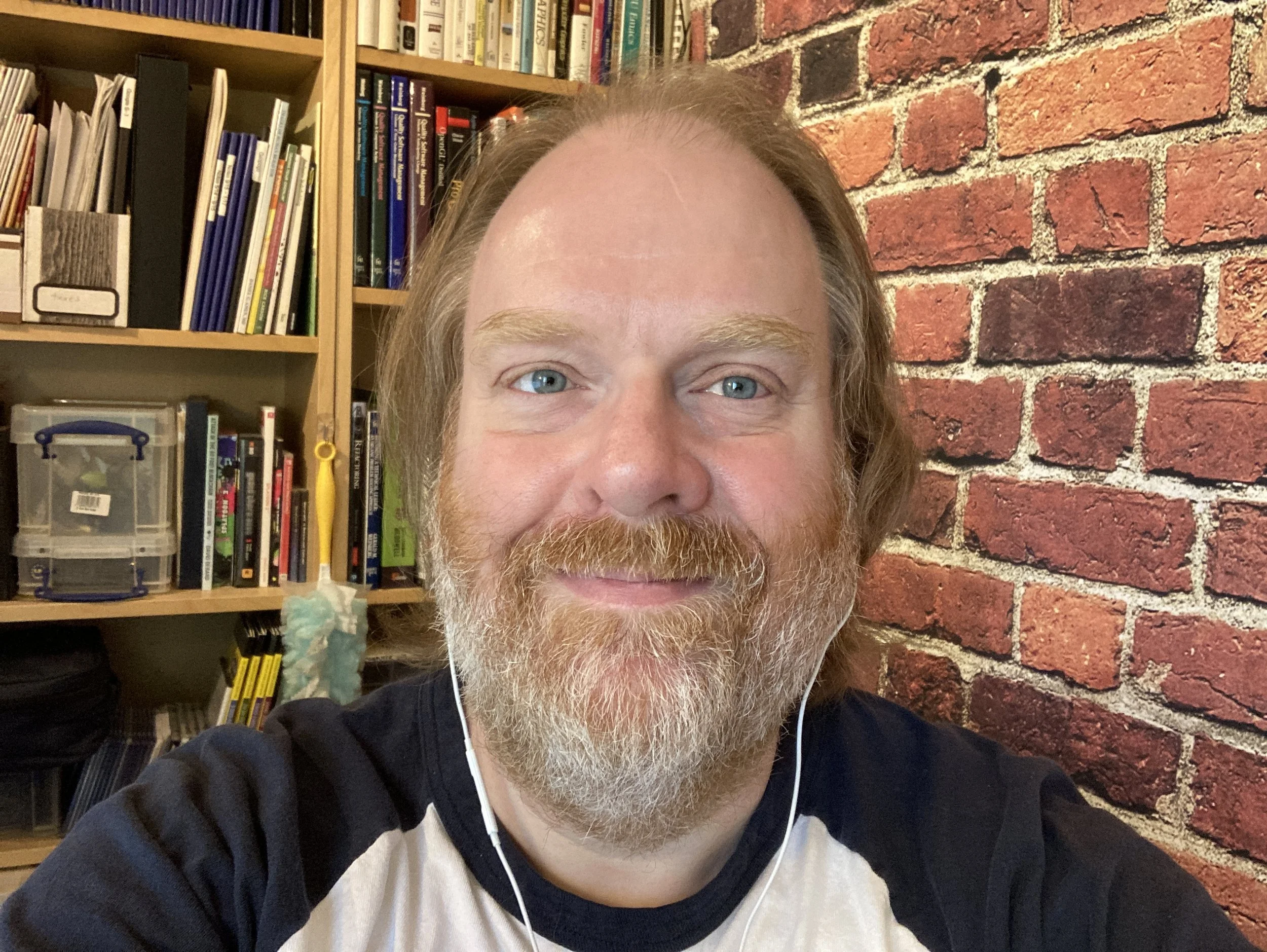 Photo of John Brewer with bookcase behind and brick wall on the right