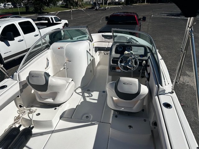 View of the cockpit of a white motorboat with two captain seats, steering wheel, and dashboard, parked in a lot with other vehicles.