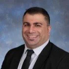 Man in a suit with a tie, smiling against a blue background.