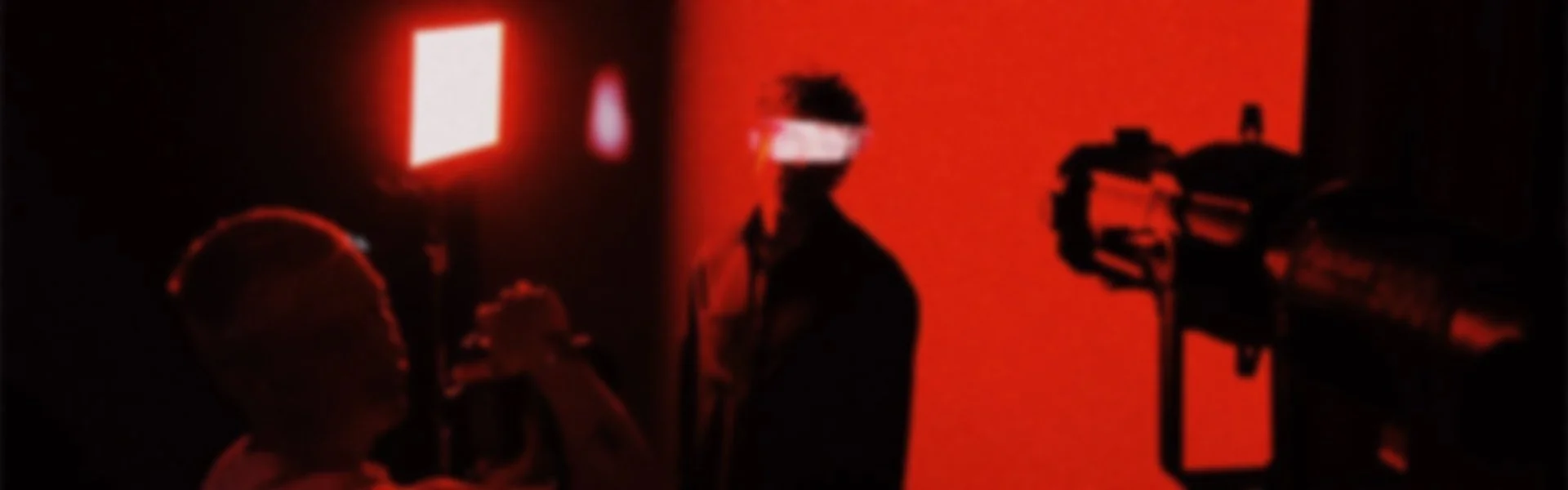 Menschen in einem dunklen Raum bei rotem Licht, einer trägt eine VR-Brille, mit Filmkamera für eine Aufnahme