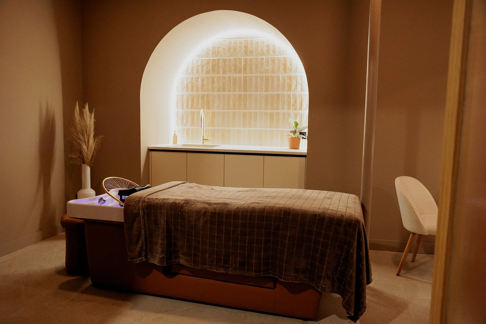 Salle dédiée au Head Spa, avec une ambiance chaleureuse. Au centre, une table et son matelas pour s'allonger. Au bout, l'arceau pour les jets d'eau