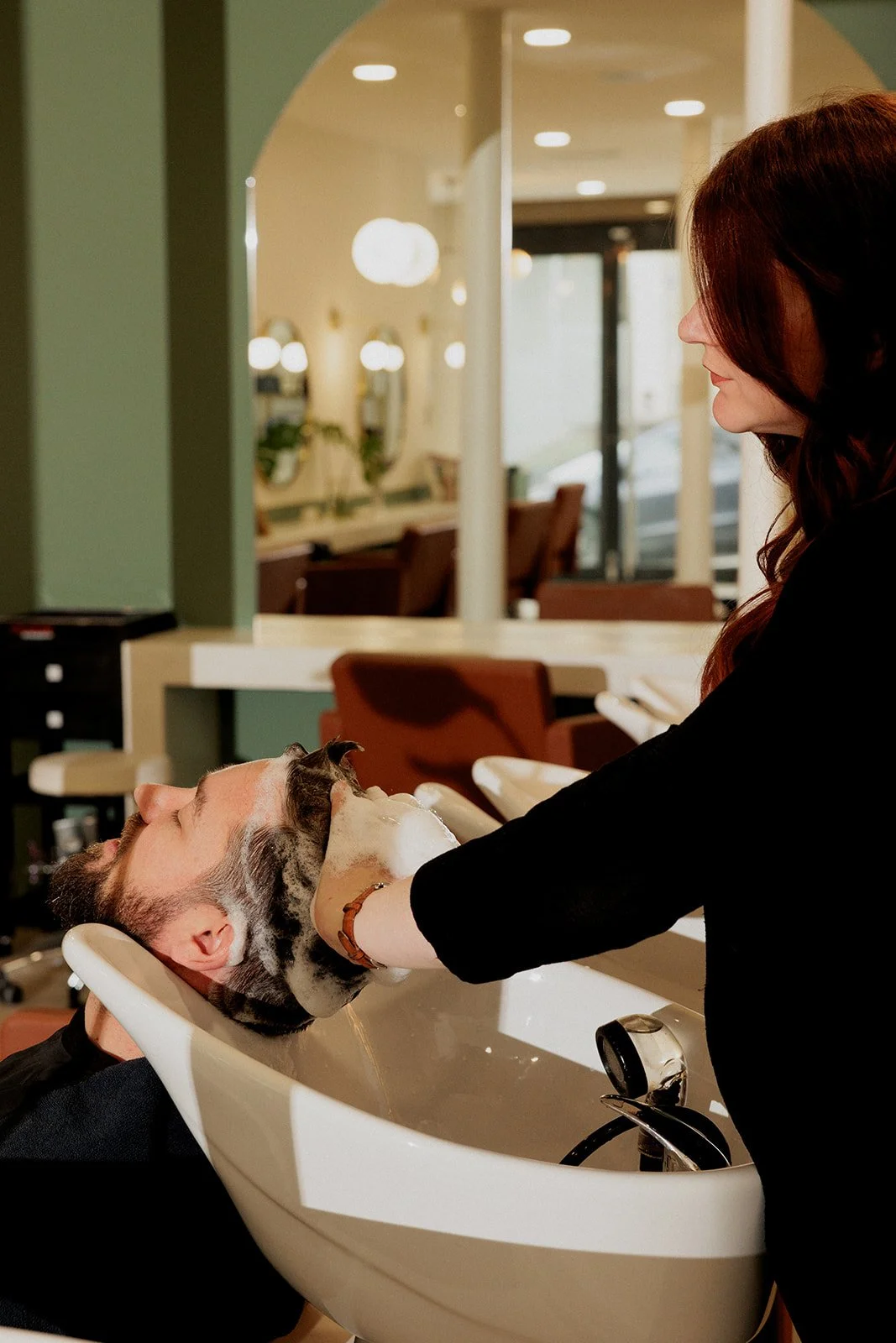 Arielle fait un shampoing à un client au bac