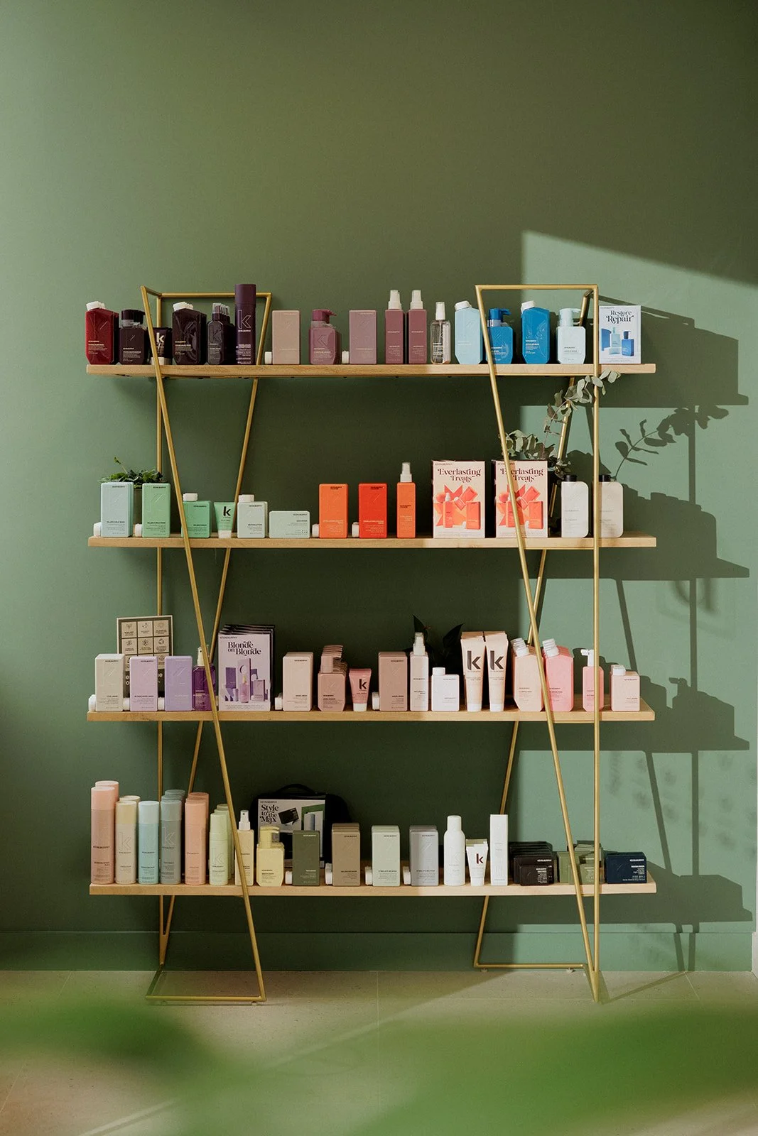 Étagère avec cadre en métal doré contenant divers produits cosmétiques, placée contre un mur vert.