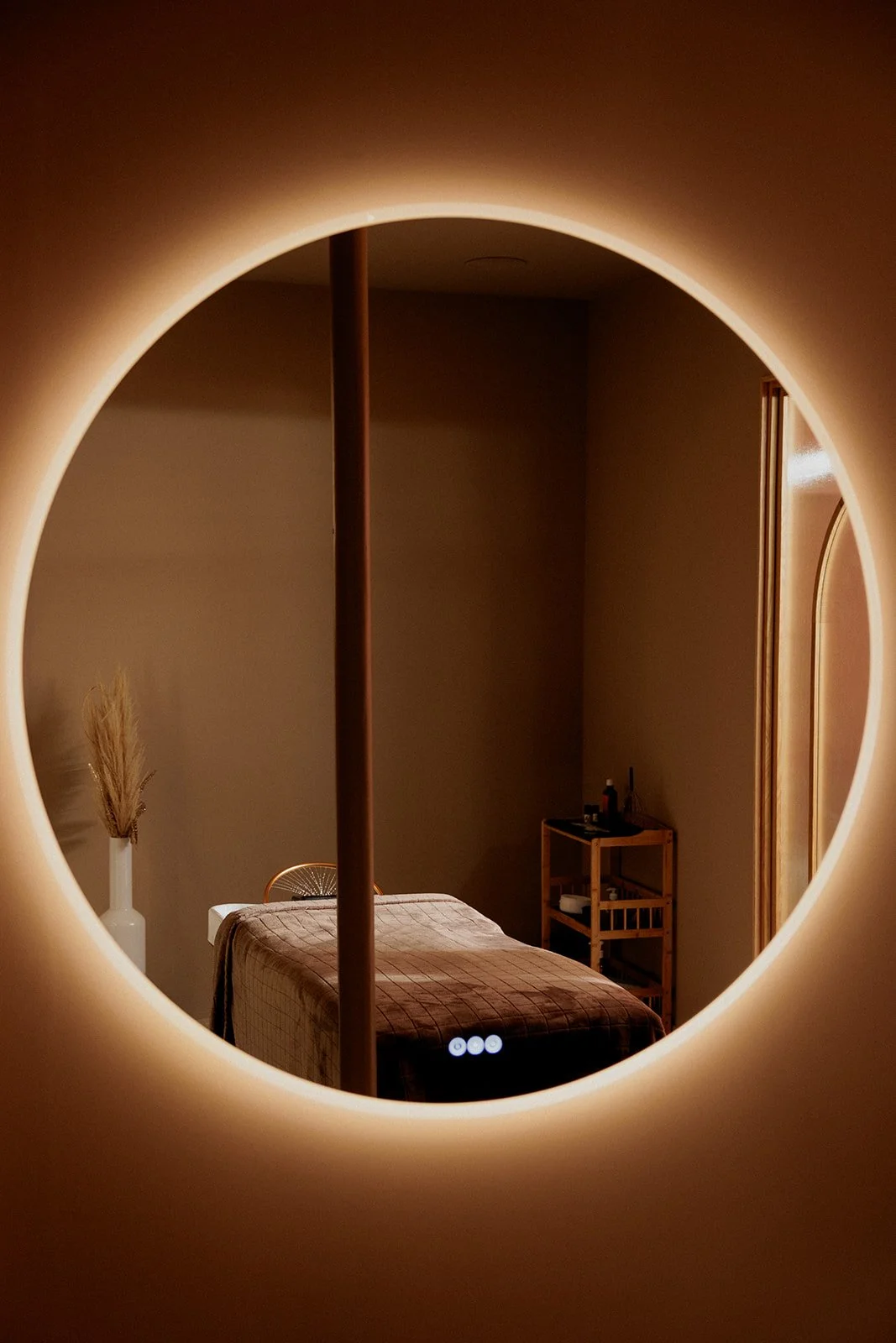 Salle Head Spa avec table et matelas vus à travers un miroir rond LED.