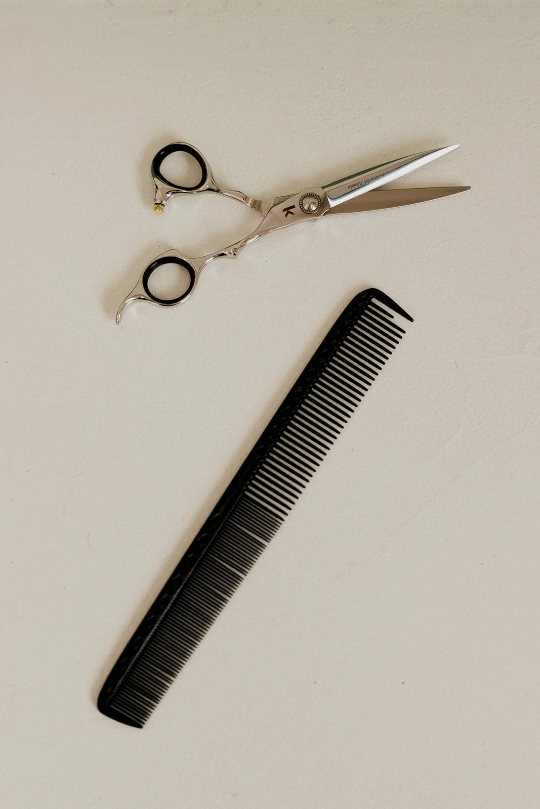 Une paire de ciseaux de coiffure, un peigne noir à dents fines, et une paire de ciseaux de salon de coiffure avec des manches en métal et des ciseaux longs et pointus, tous disposés sur une surface blanche.