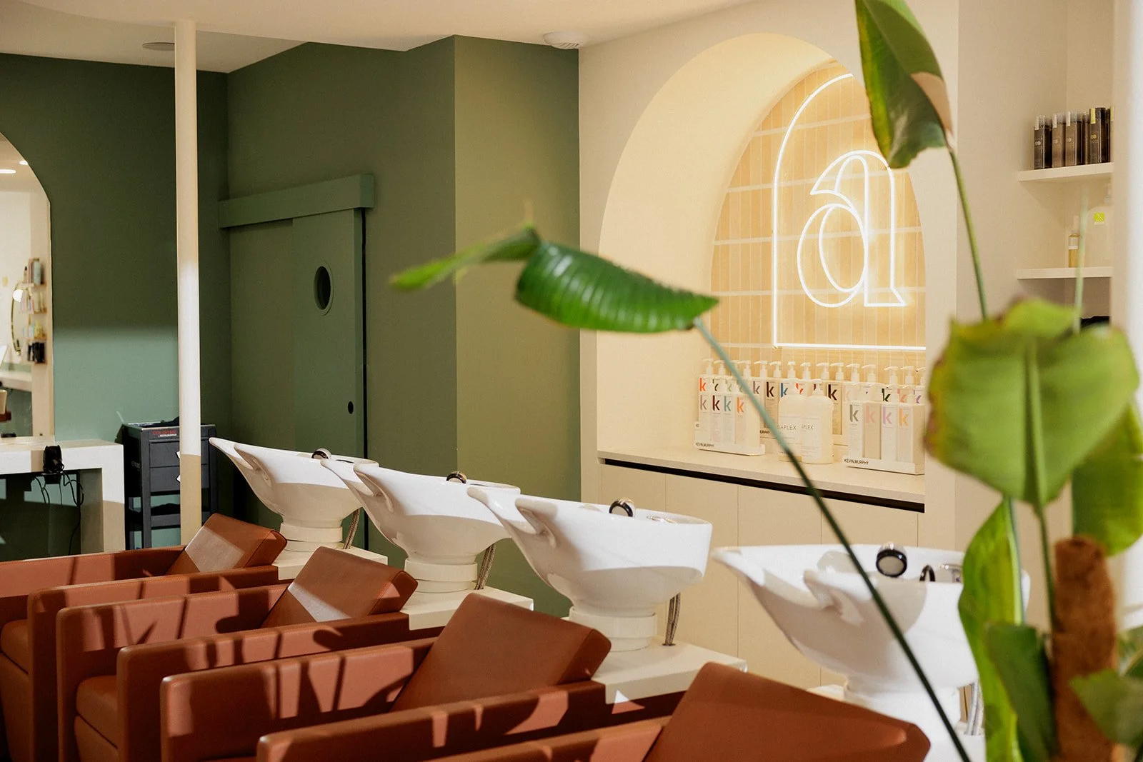 Intérieur du salon de coiffure Arielle avec les bacs à shampoing. En arrière-plan, un mur vert, et une arche avec un néon avec le "a" du logo Arielle