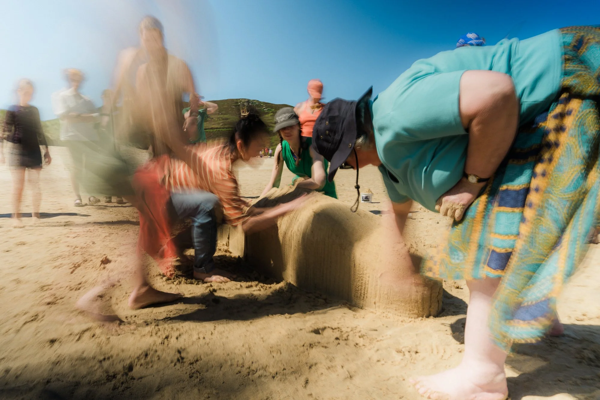 A group of people work together to gently smooth and create a sand whale, as part of Keening - Song of the Stranding