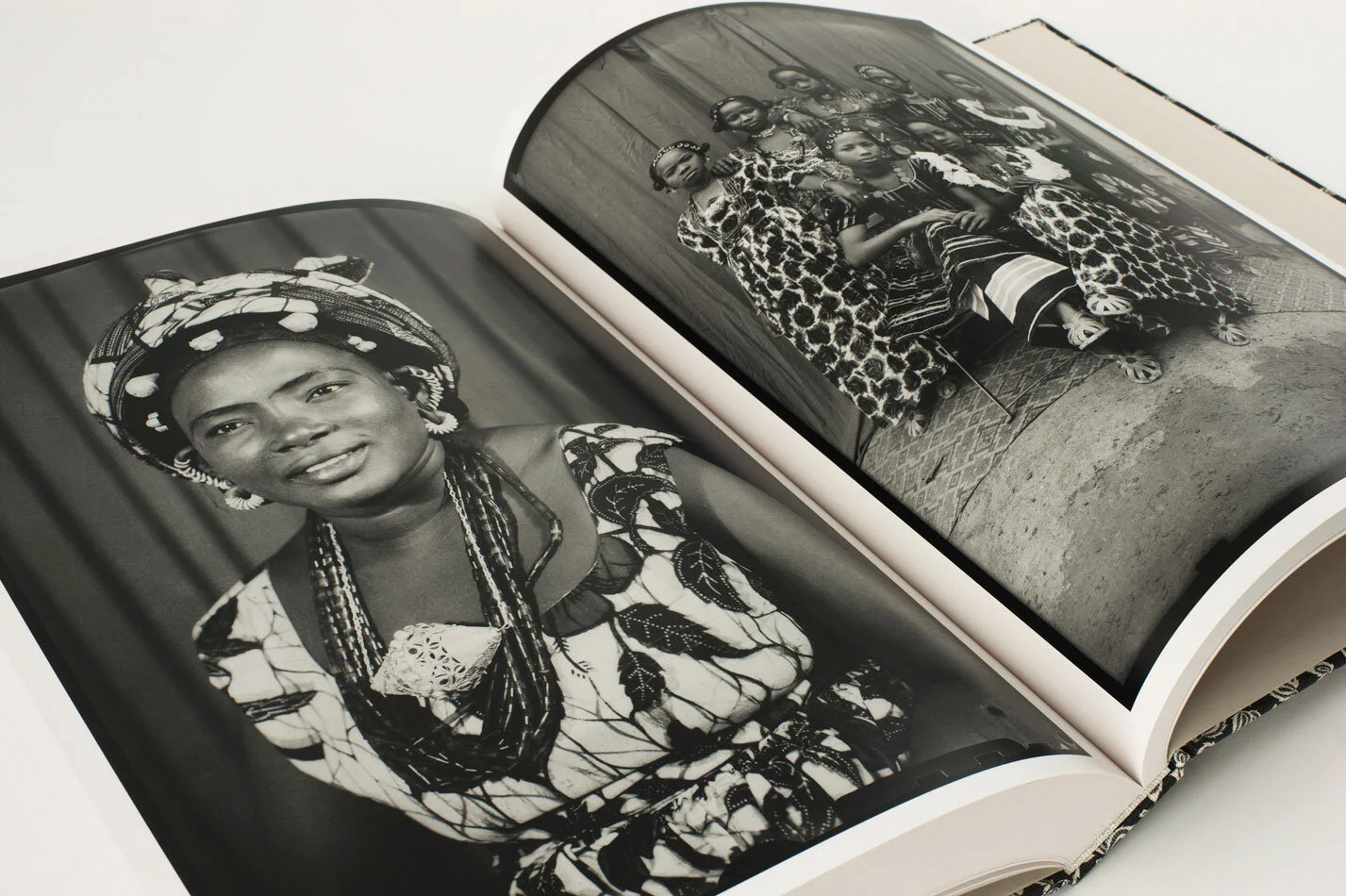 Black and white photographs by Seidou Keita, of African women in traditional dress, one in a headwrap and beads, and the other with three women in patterned dresses standing on a brick sidewalk.