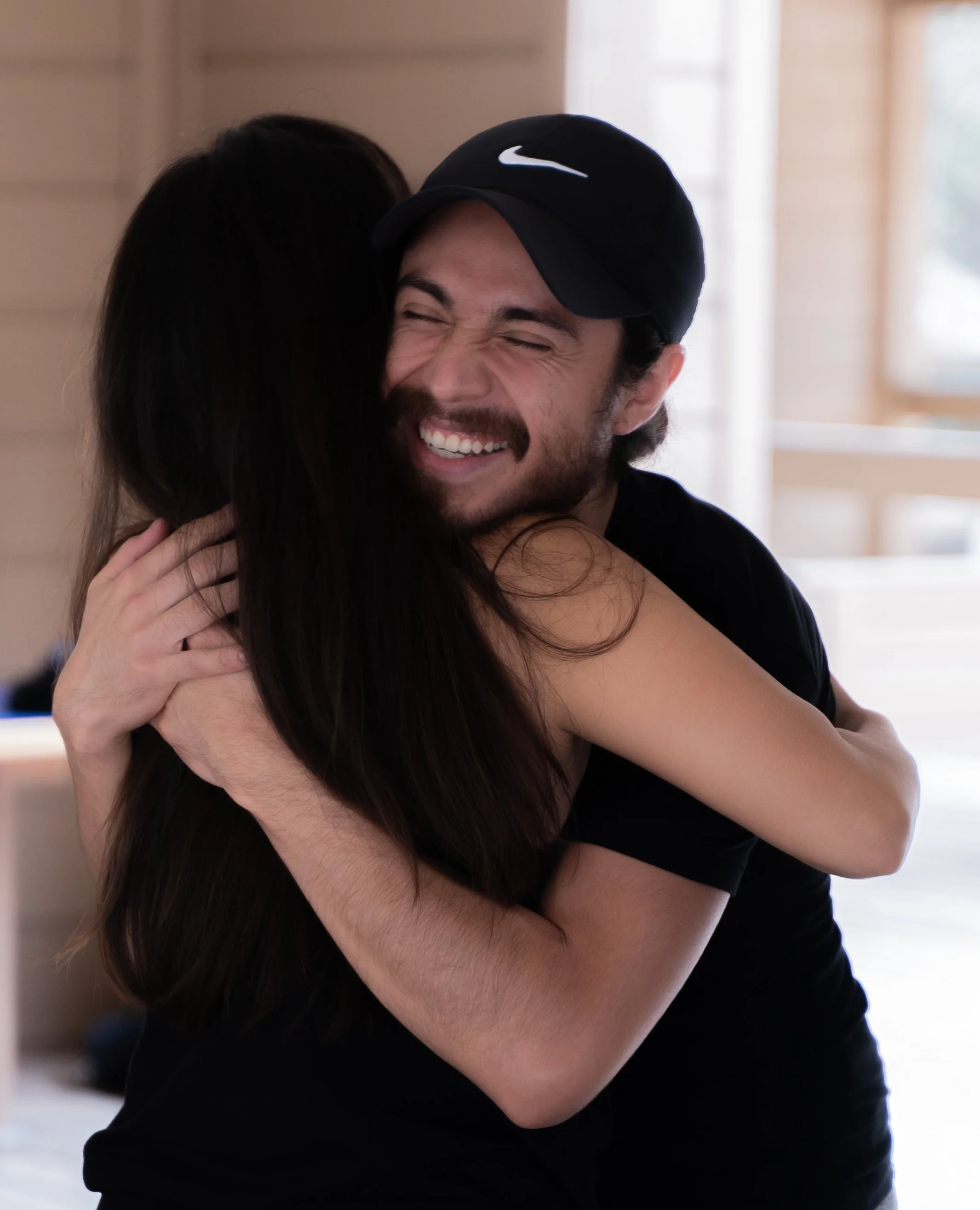 man in nike hat smiles big with eyes closed hugging woman with long black hair at a retreat by photographer Lenee Love
