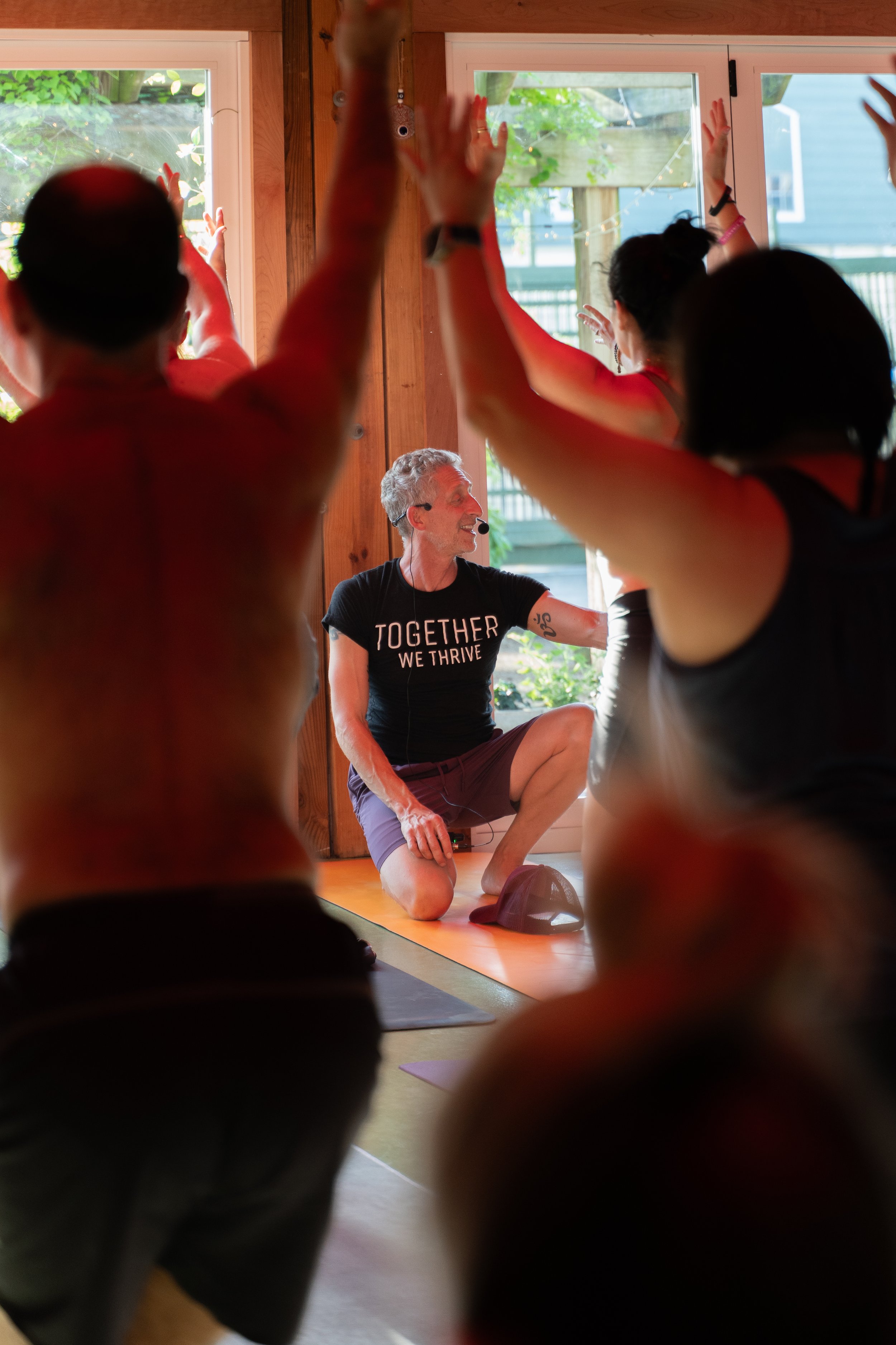 yoga teacher seen teaching at the front of the room through the arms of students holding warrior one at valor in houston by photographer Lenee Love