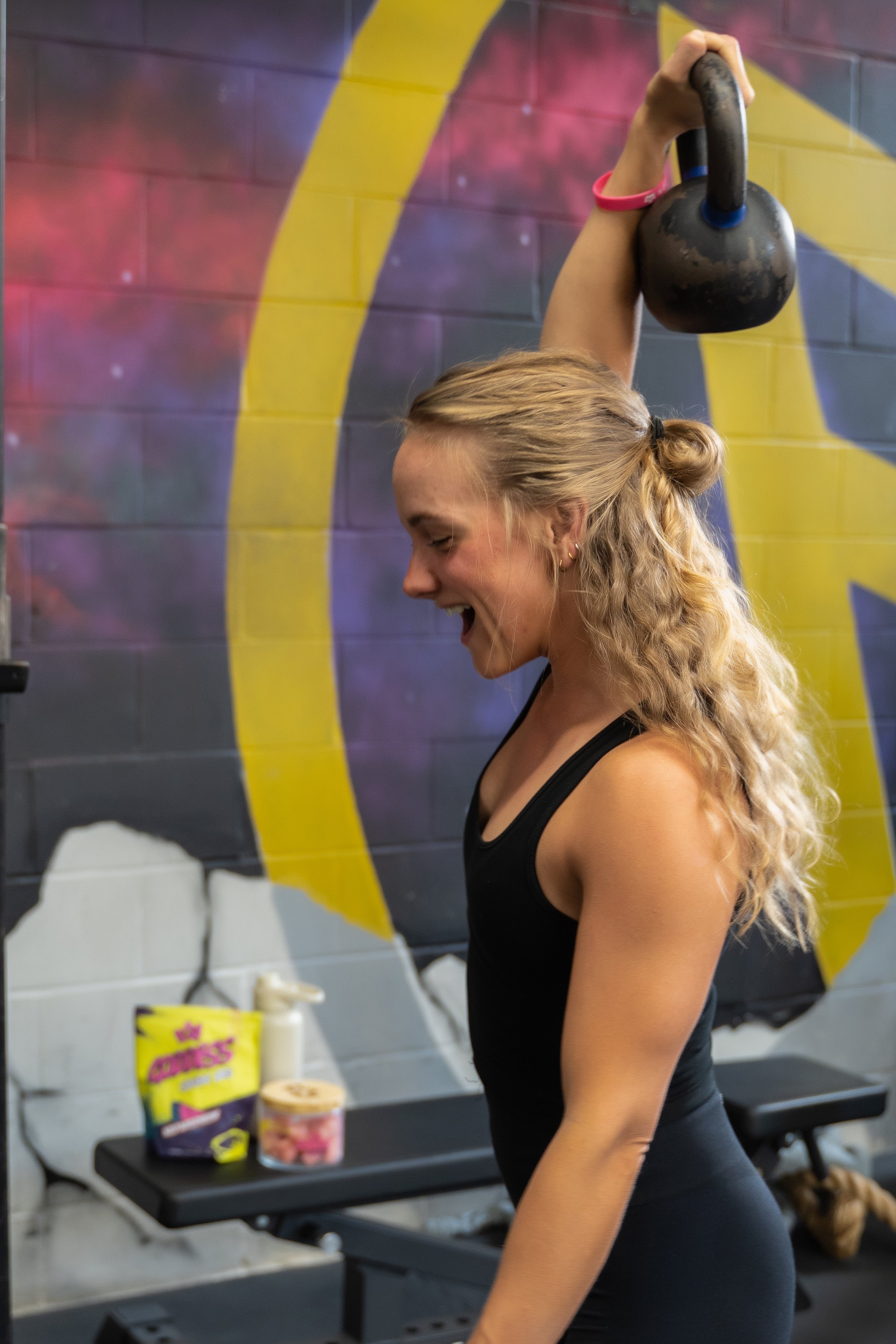 woman in the gym with kettle bell overhead and primal queen supplements in the background by fitness product photographer Lenee Love