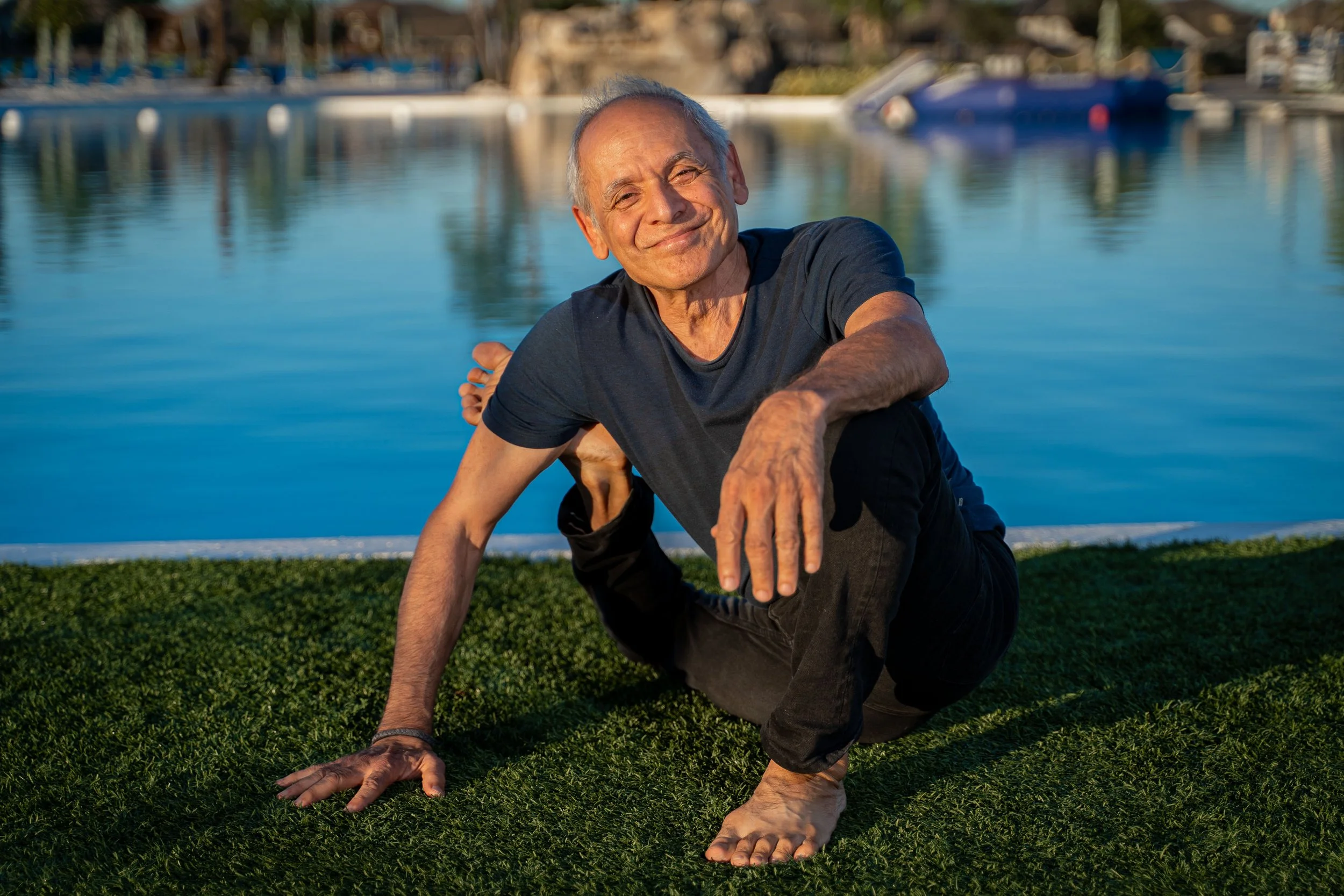 elder man in the sunshine doing a difficult yoga pose with a smile by the water by yoga photographer Lenee Love