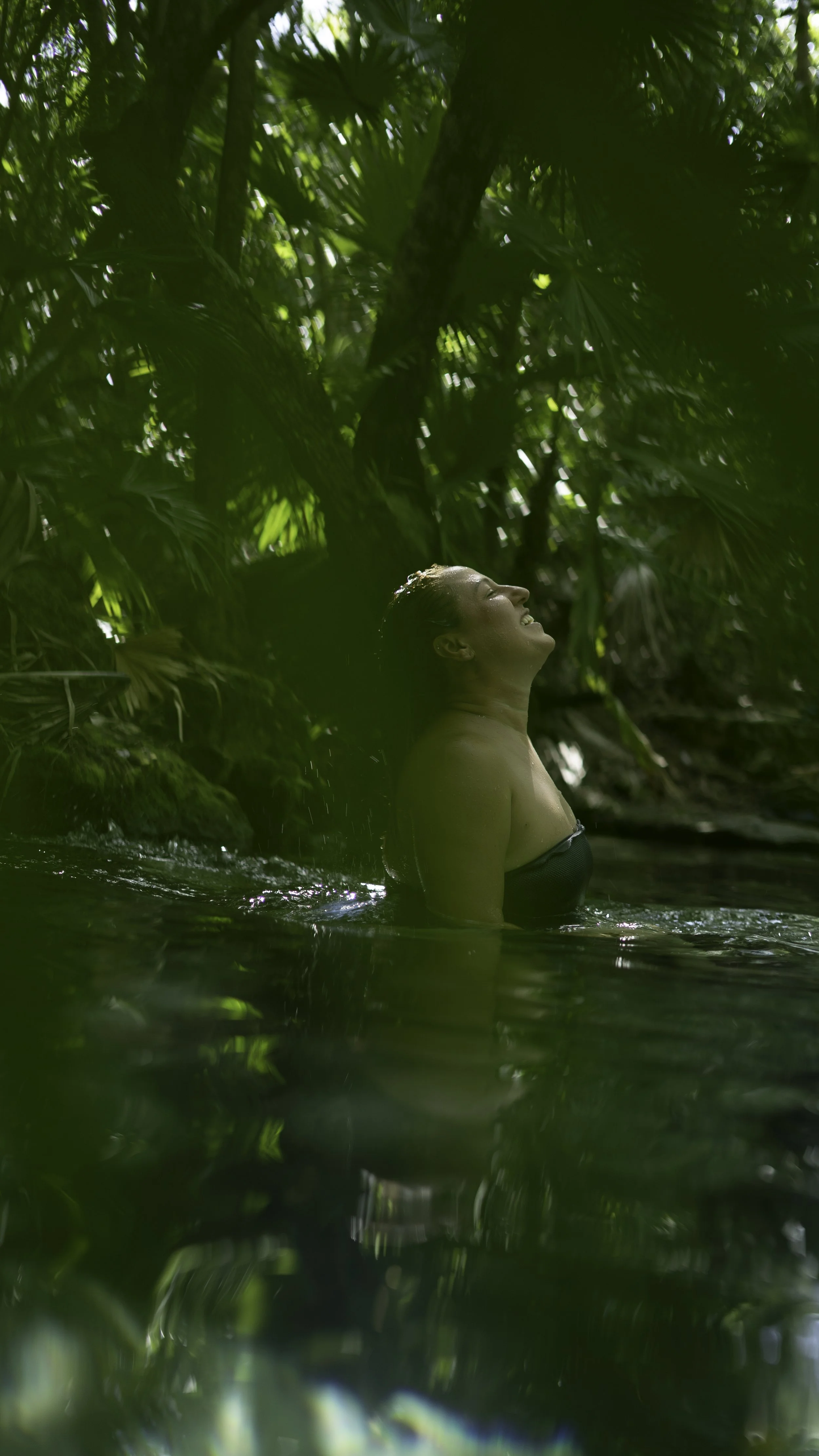 side profile of a woman in cenote shot through green leaves in Tulum by retreat photographer Lenee Love