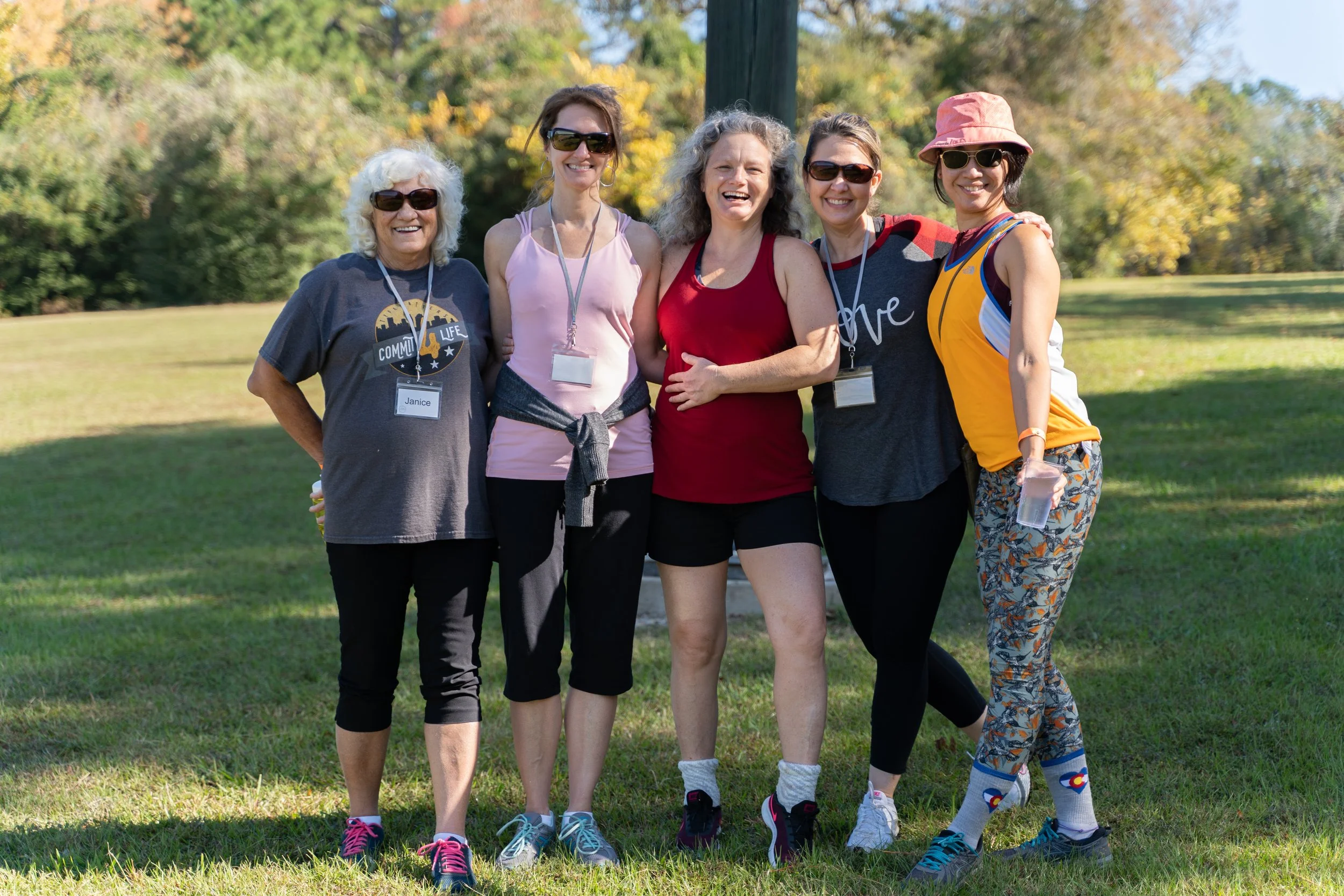 5 happy women pose full body at a retreat hike outdoors surrounded by green grass and trees by photographer Lenee Love