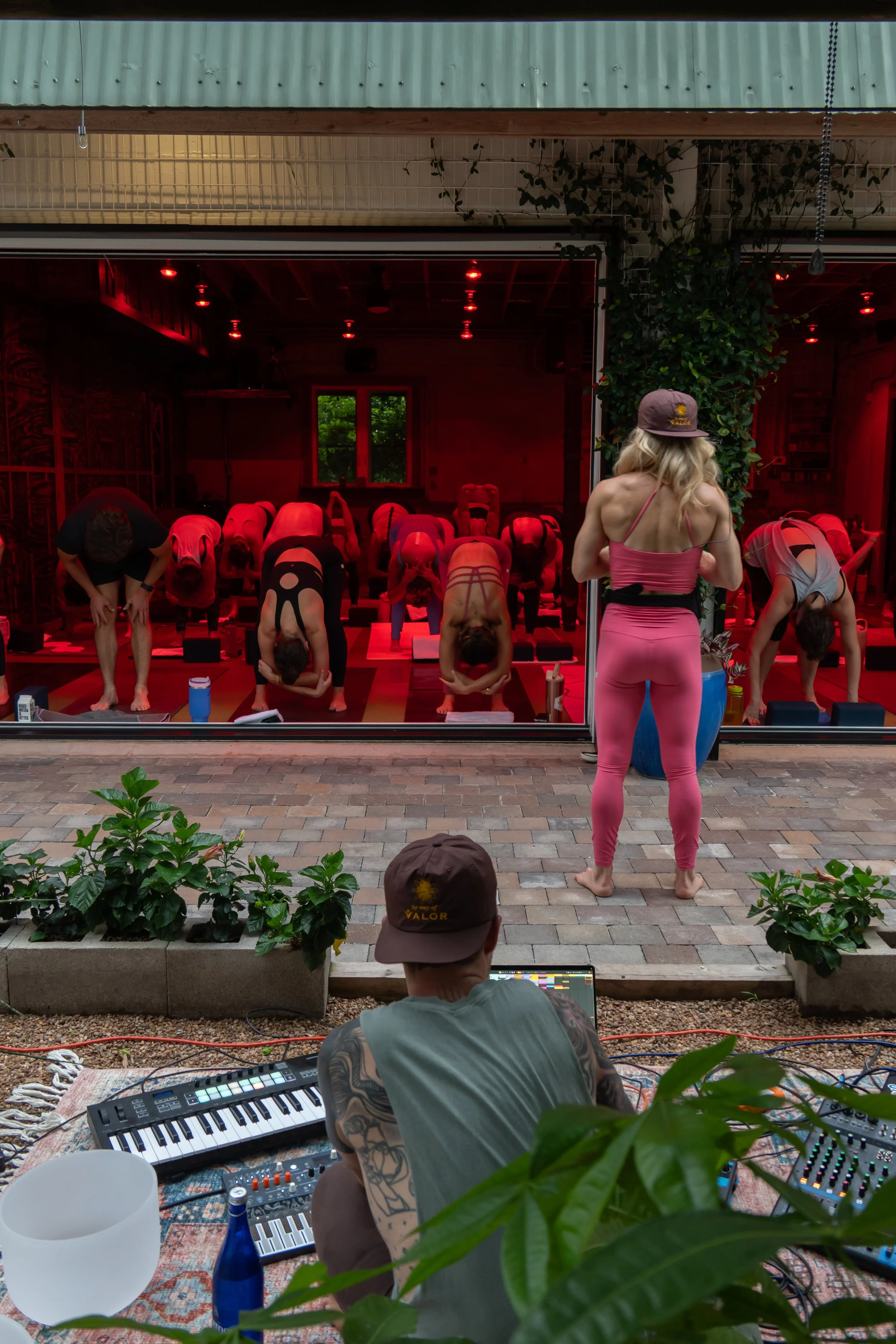 yoga class in forward fold under sauna space red light bulbs with teacher standing at the front of the class and live music in the garden by photographer Lenee Love