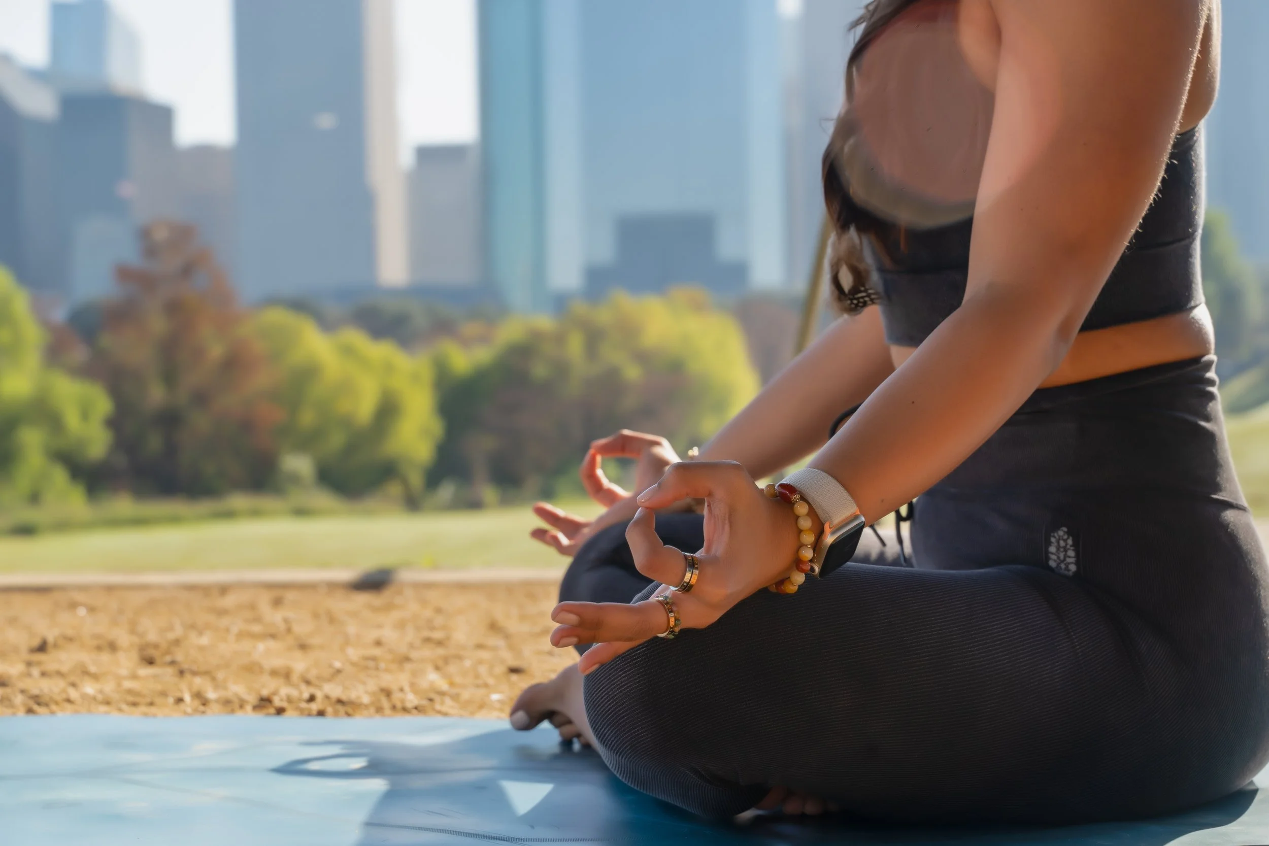 close up shot of woman sitting in meditation with a mudra and the houston skyline backdrop by photographer Lenee Love