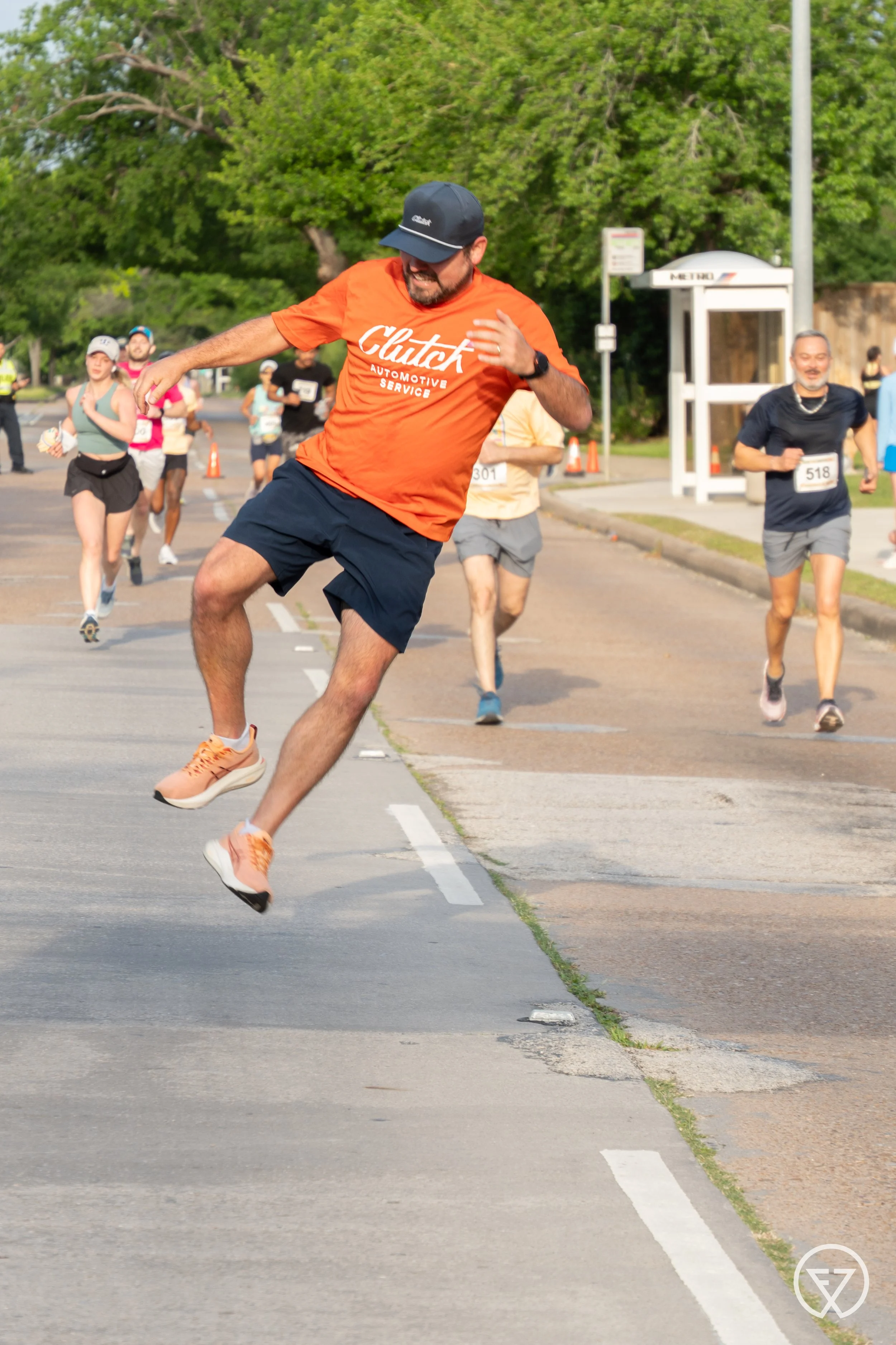 man in orage clutch shirt clicking his heels in the air during 5k run by fitness photographer Lenee Love