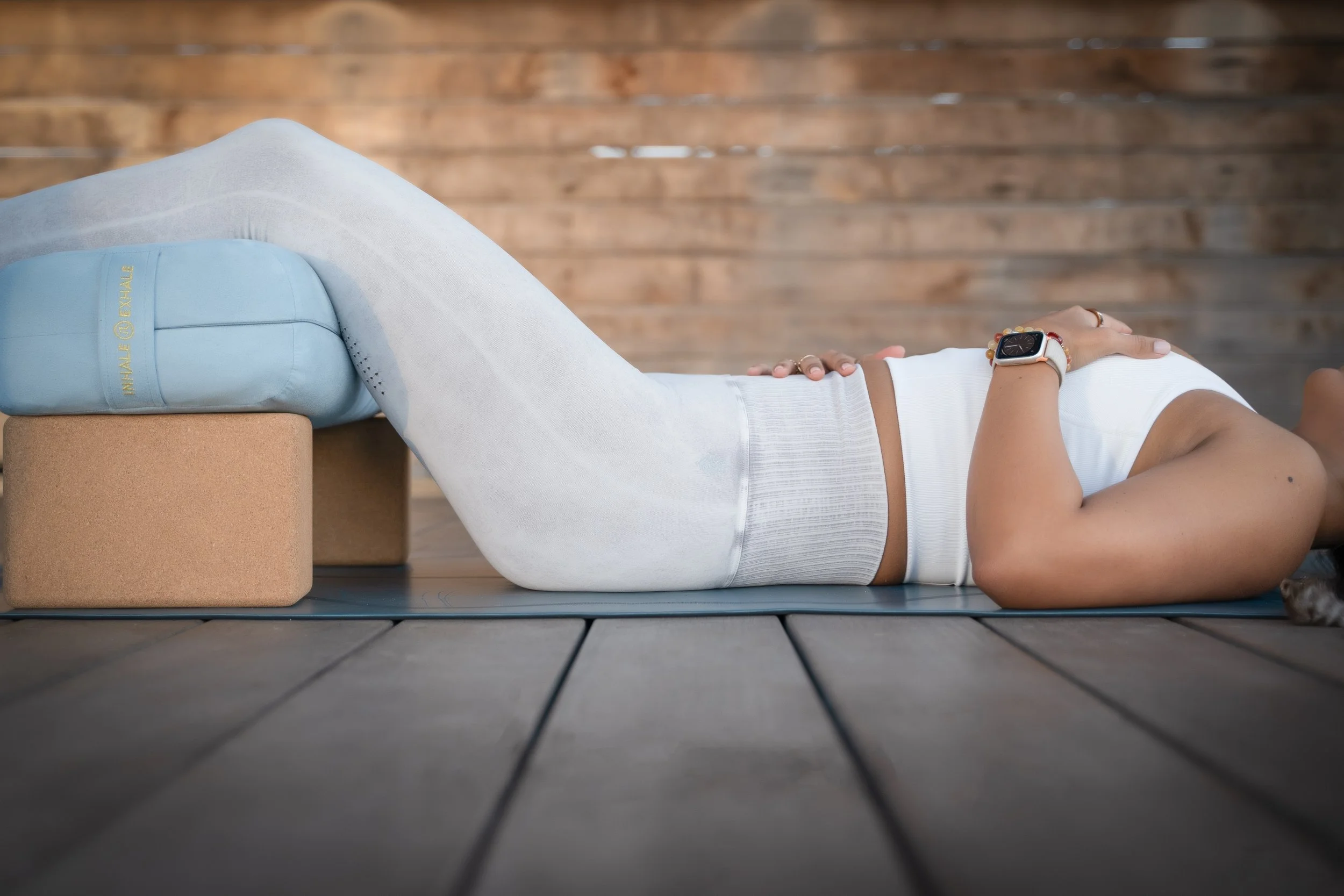 woman lying in a restorative yoga pose with blocks and bolsters hands on heart and belly by photographer Lenee Love