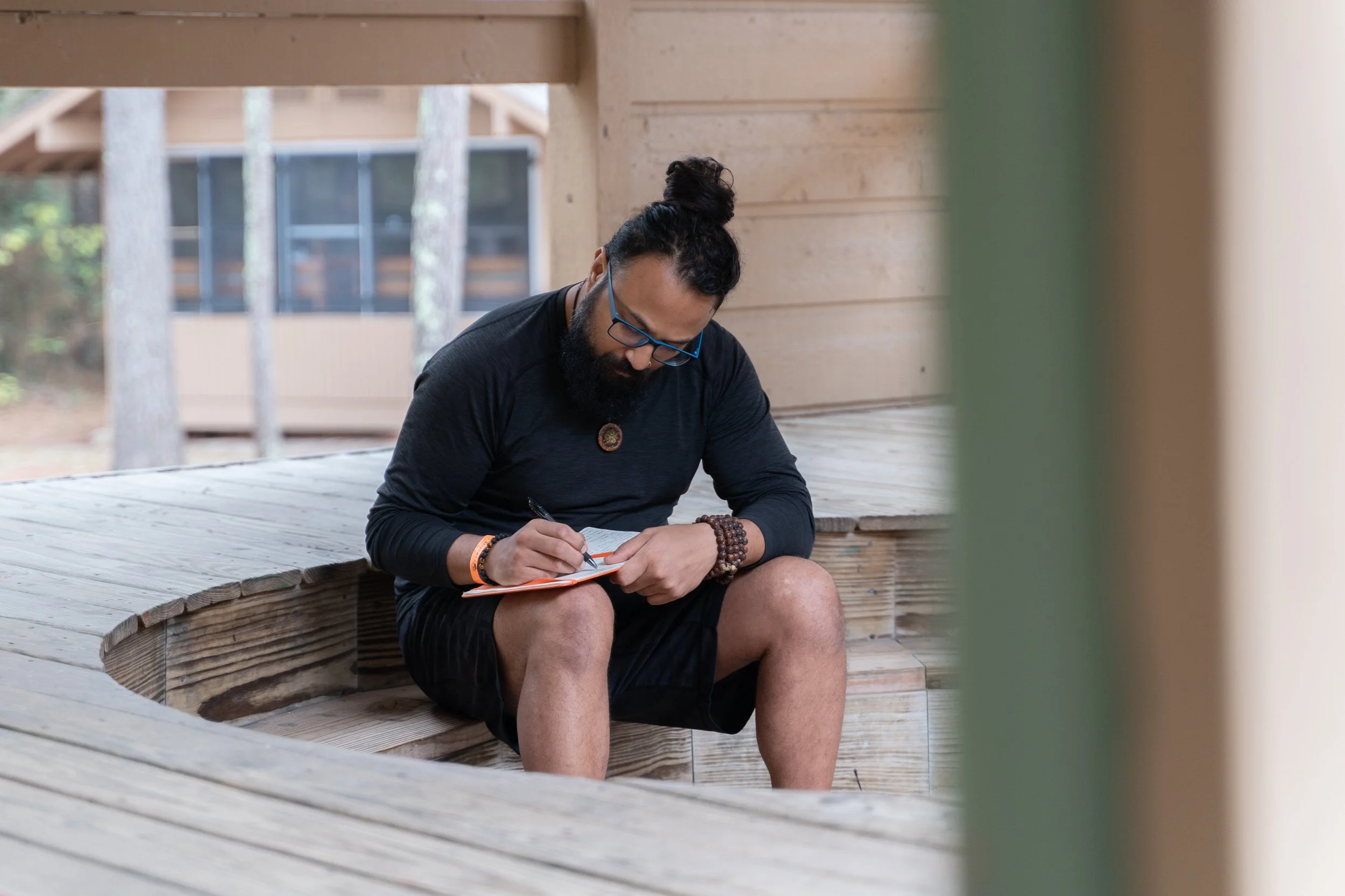 man in atheletic wear with a man bun and glasses journals on an outdoor deck peacefully by retreat photographer Lenee Love