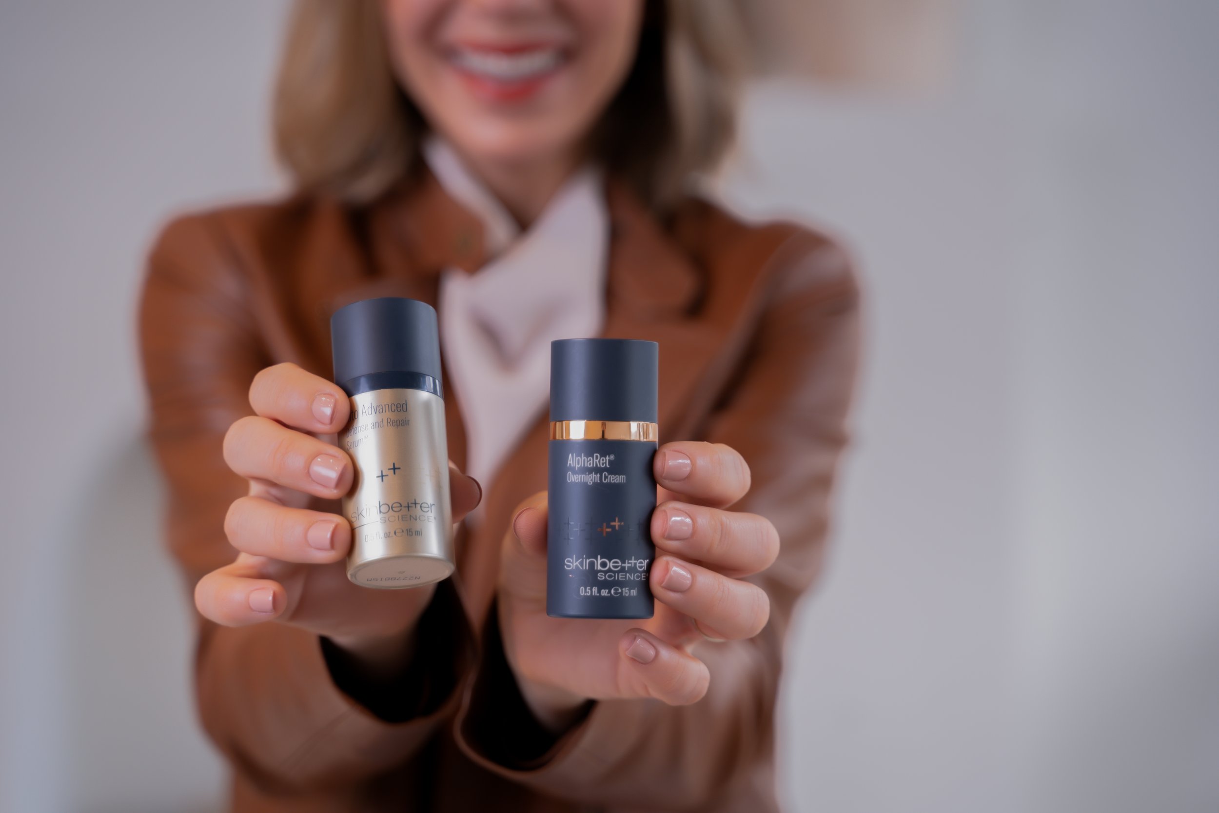 woman in a brown leather jacket is out of focus and holds out two skin better science products by product photographer Lenee Love